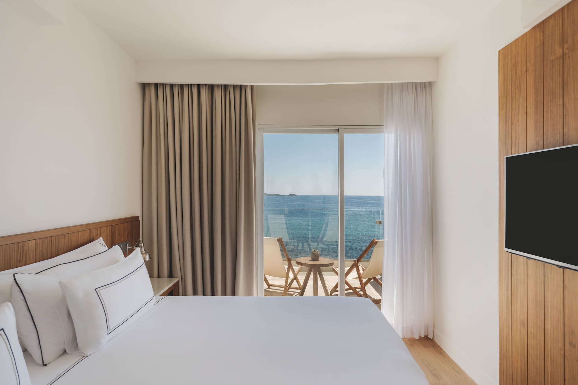 Modern hotel bedroom with sea view balcony and wooden accents.