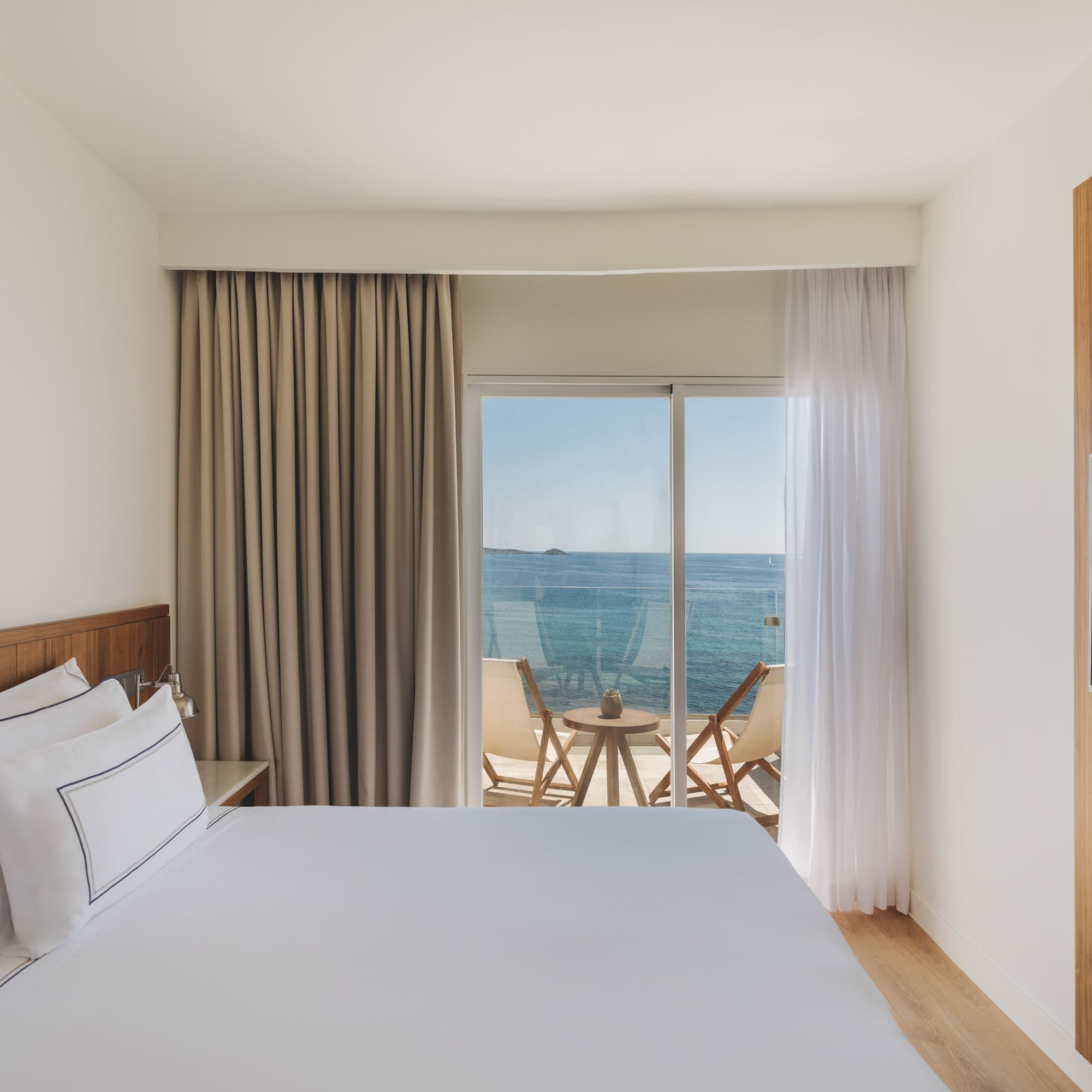 Modern hotel bedroom with sea view balcony and wooden accents.