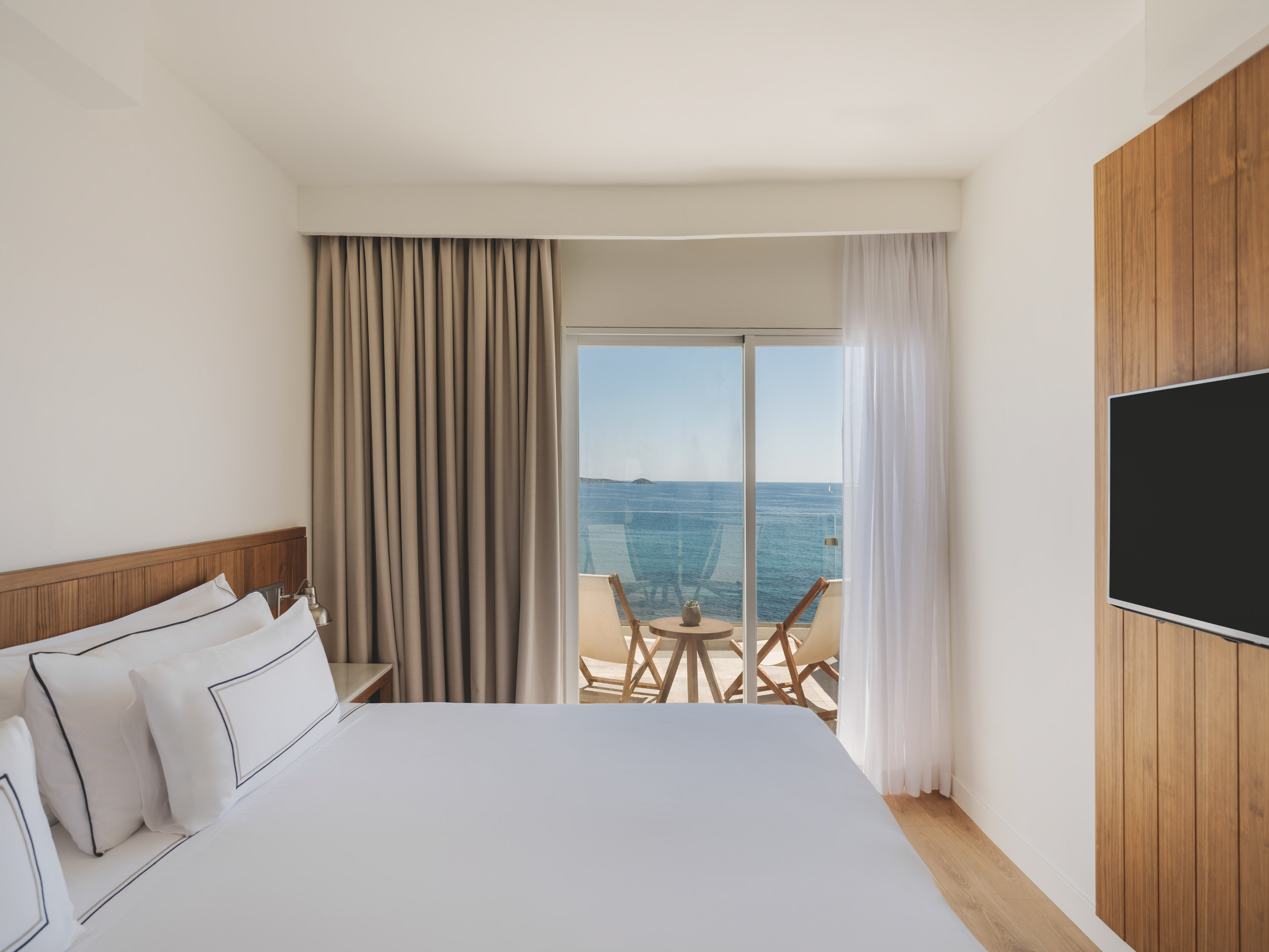 Modern hotel bedroom with sea view balcony and wooden accents.