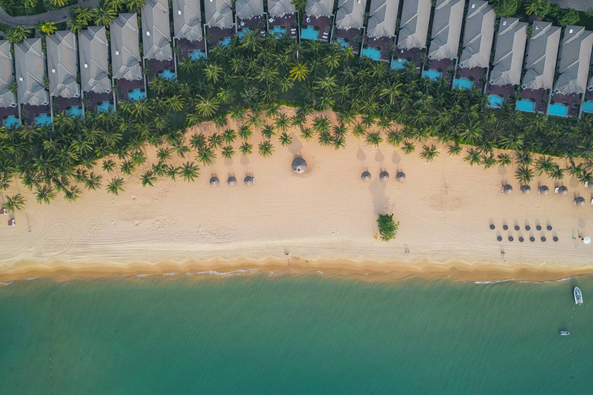 Aerial: Beach resort, villas, palm trees, sandy beach, turquoise ocean, and boat.