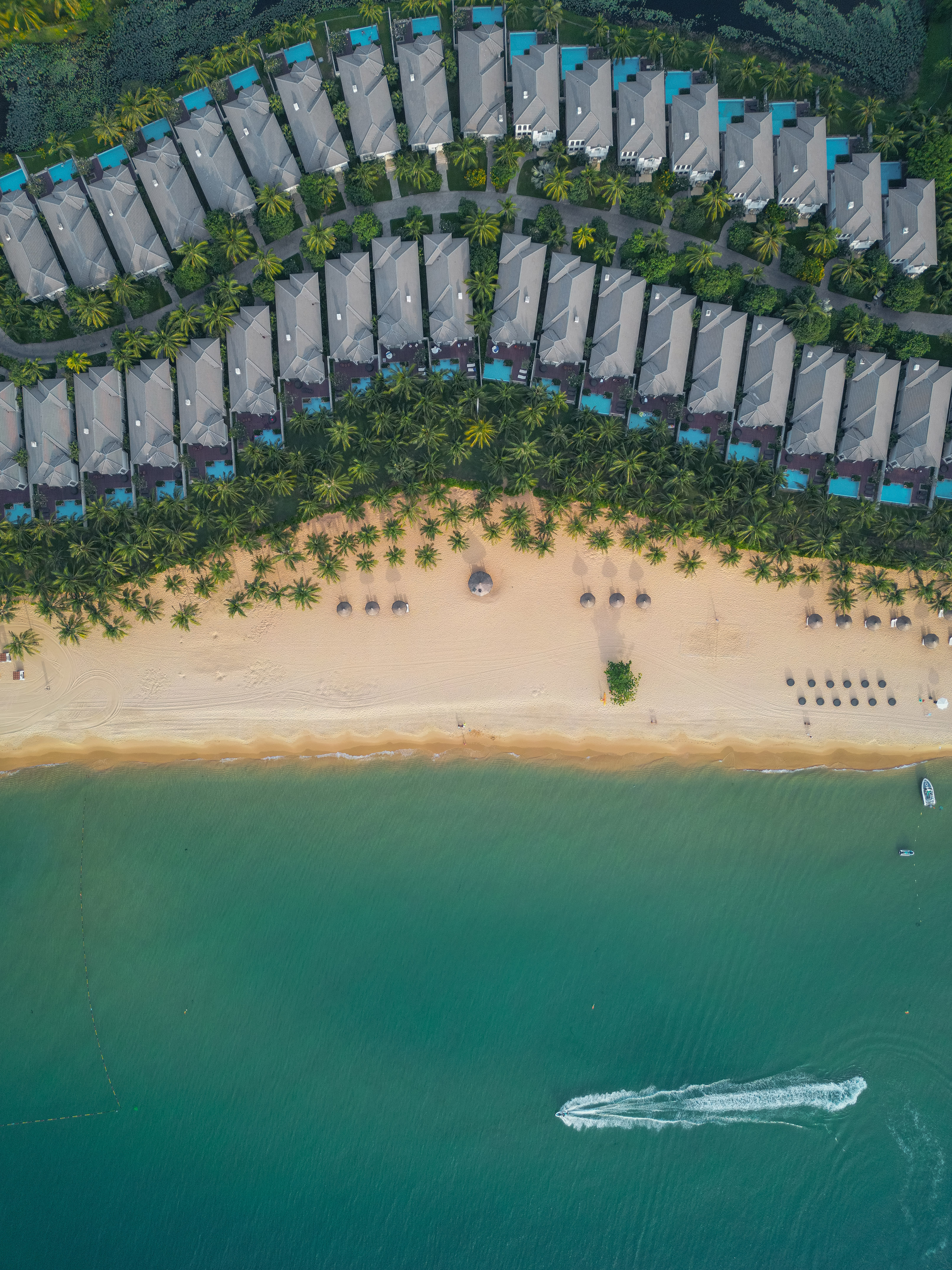 Aerial: Beach resort, villas, palm trees, sandy beach, turquoise ocean, and boat.