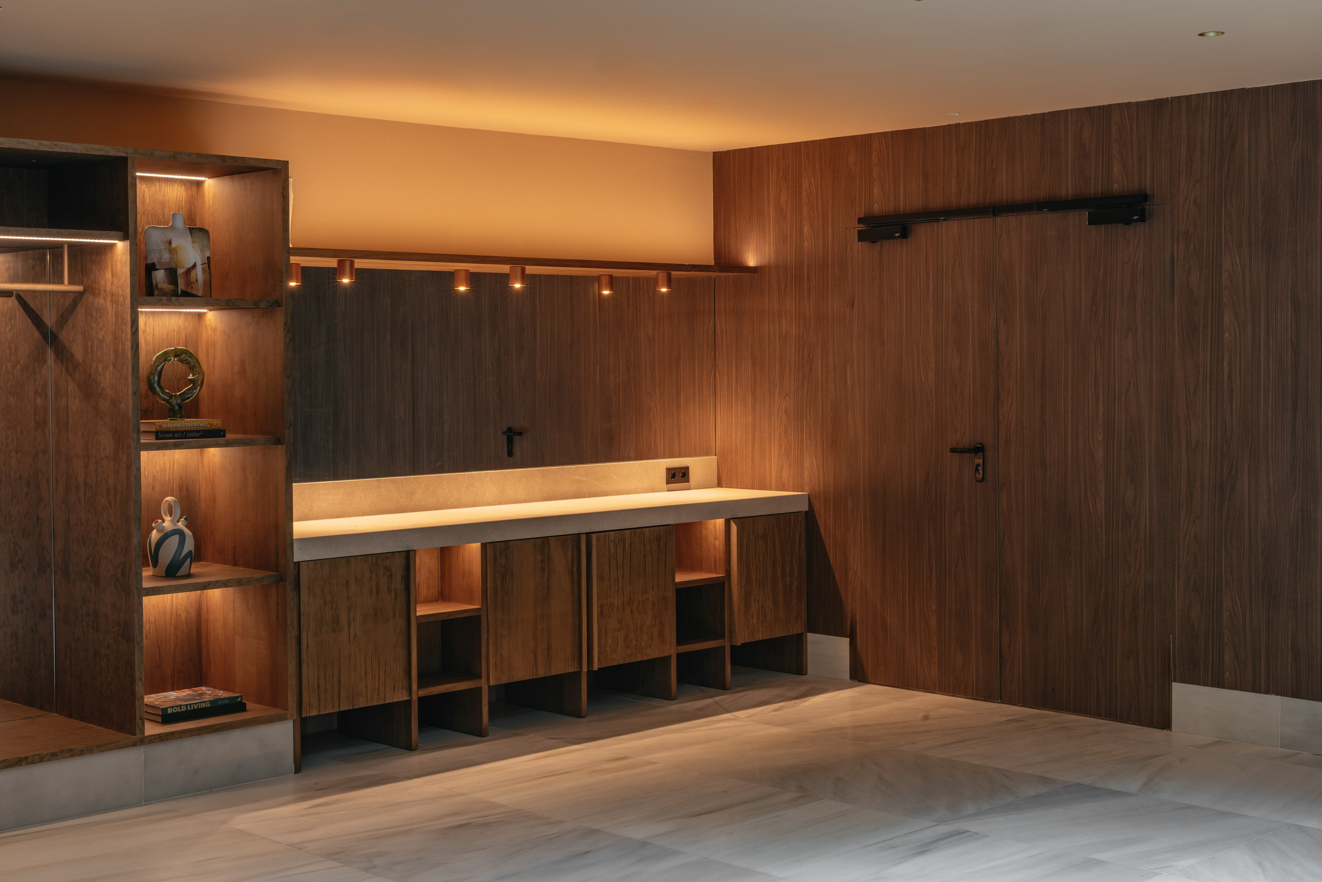 Modern interior with wood paneling, illuminated shelves, concrete counter, marble floor.
