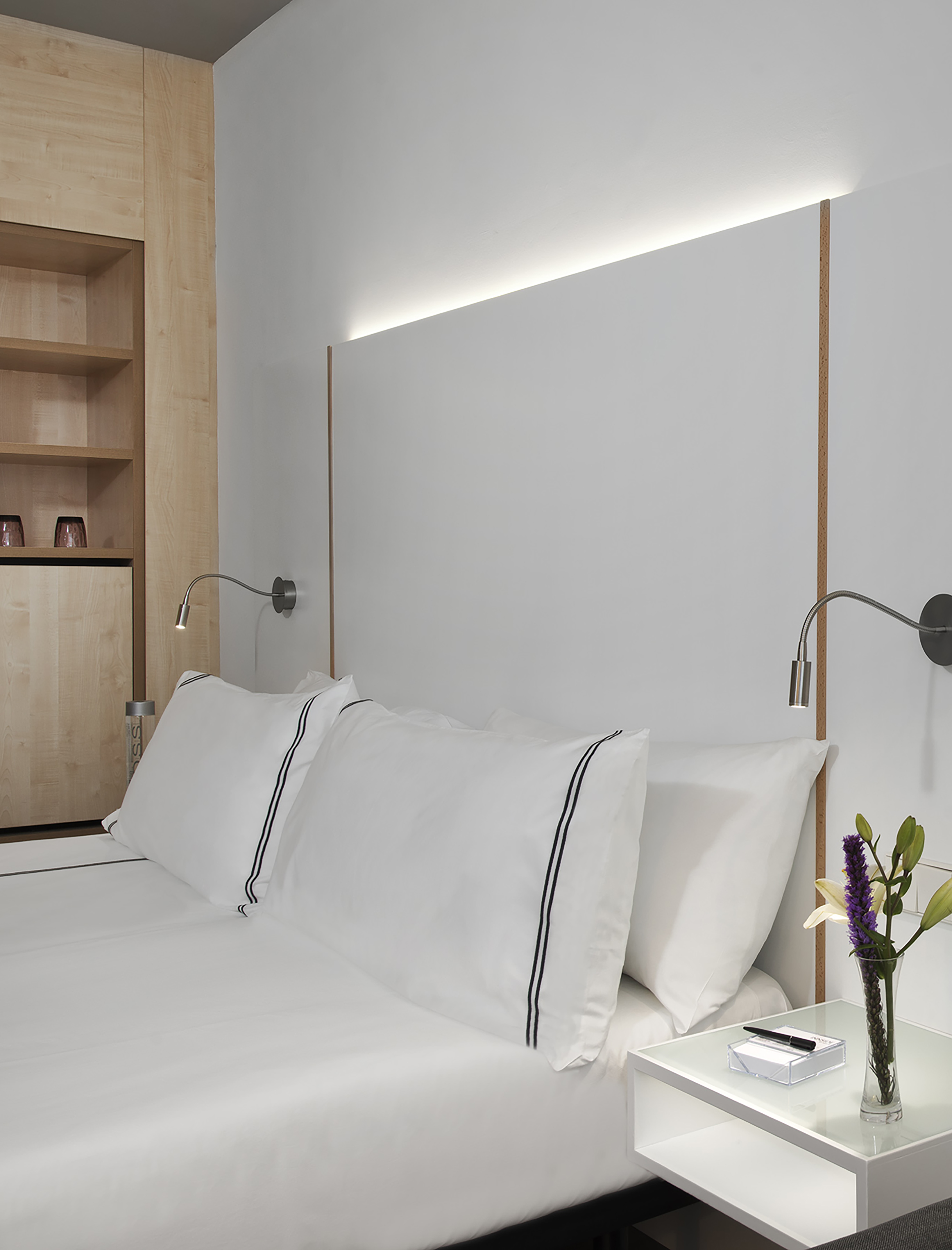 Modern hotel bedroom with white bedding, wood cabinet, and backlit headboard.