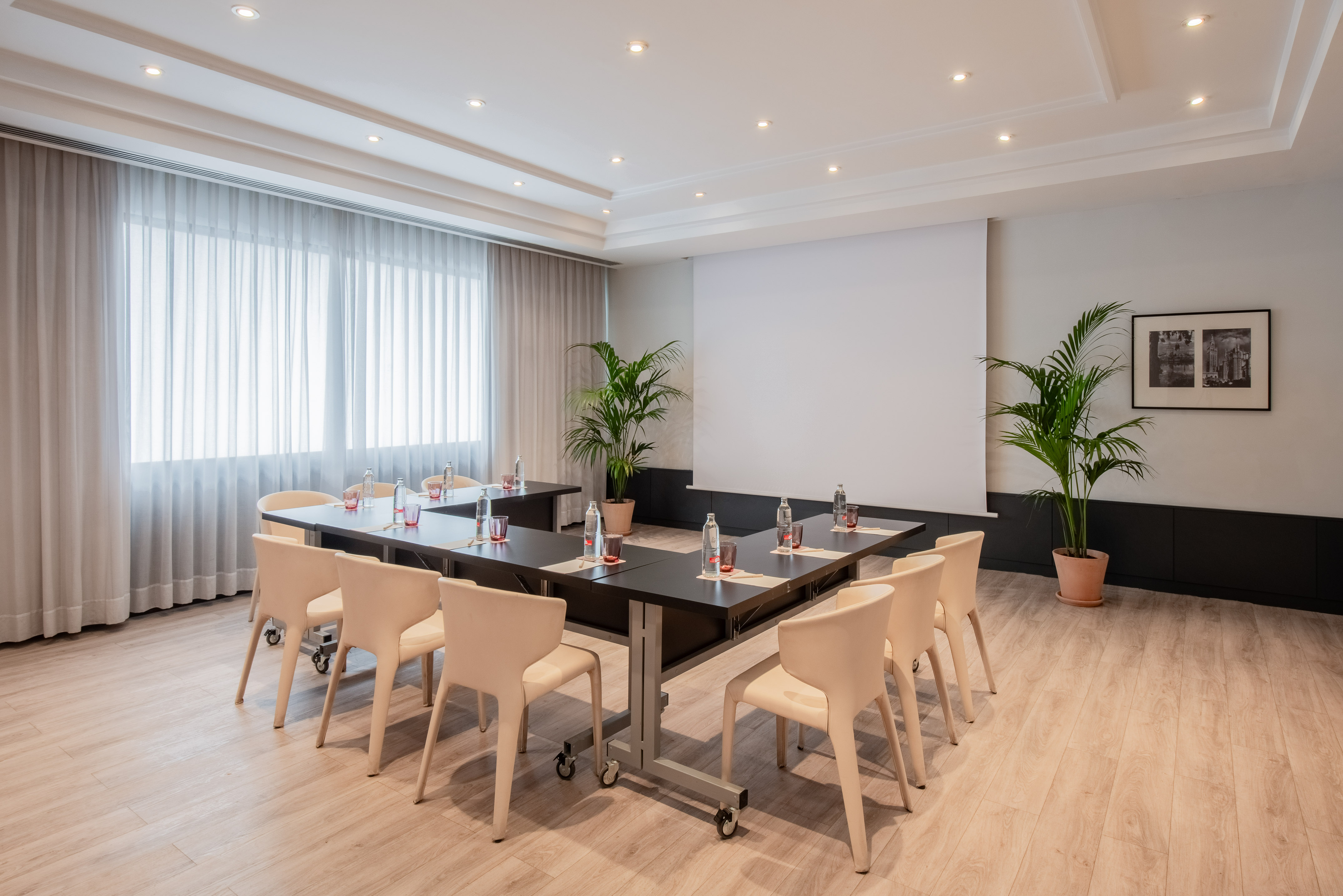 Bright modern conference room, U-shaped table, projector screen, plants.