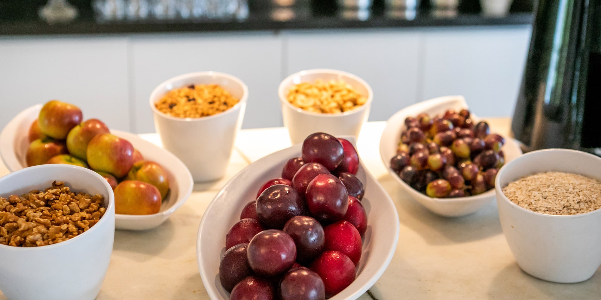 Healthy breakfast bar with fresh apples, plums, grapes, walnuts, granola, and oats.