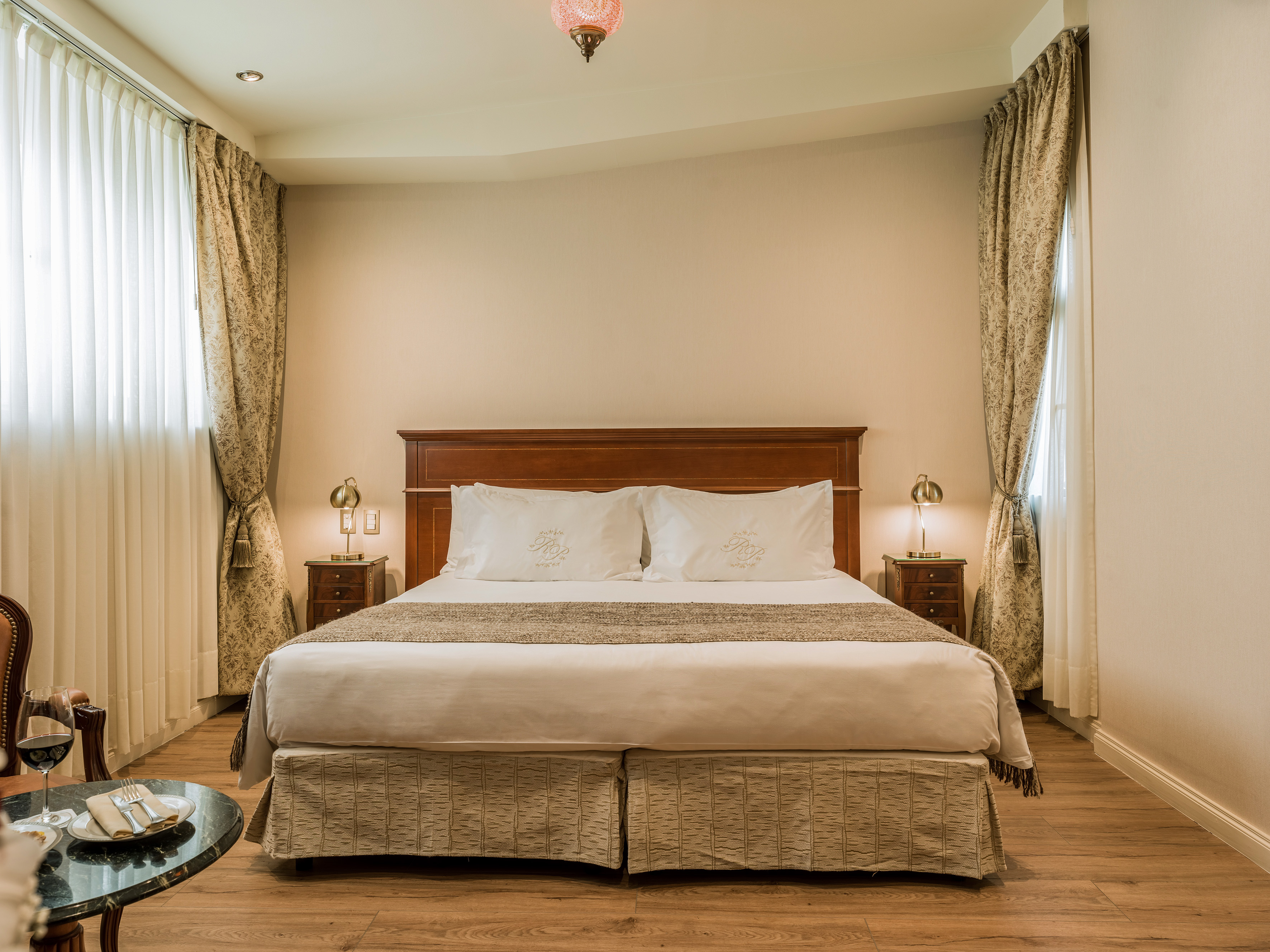 Elegant hotel bedroom with king bed, wooden furniture, and patterned curtains.