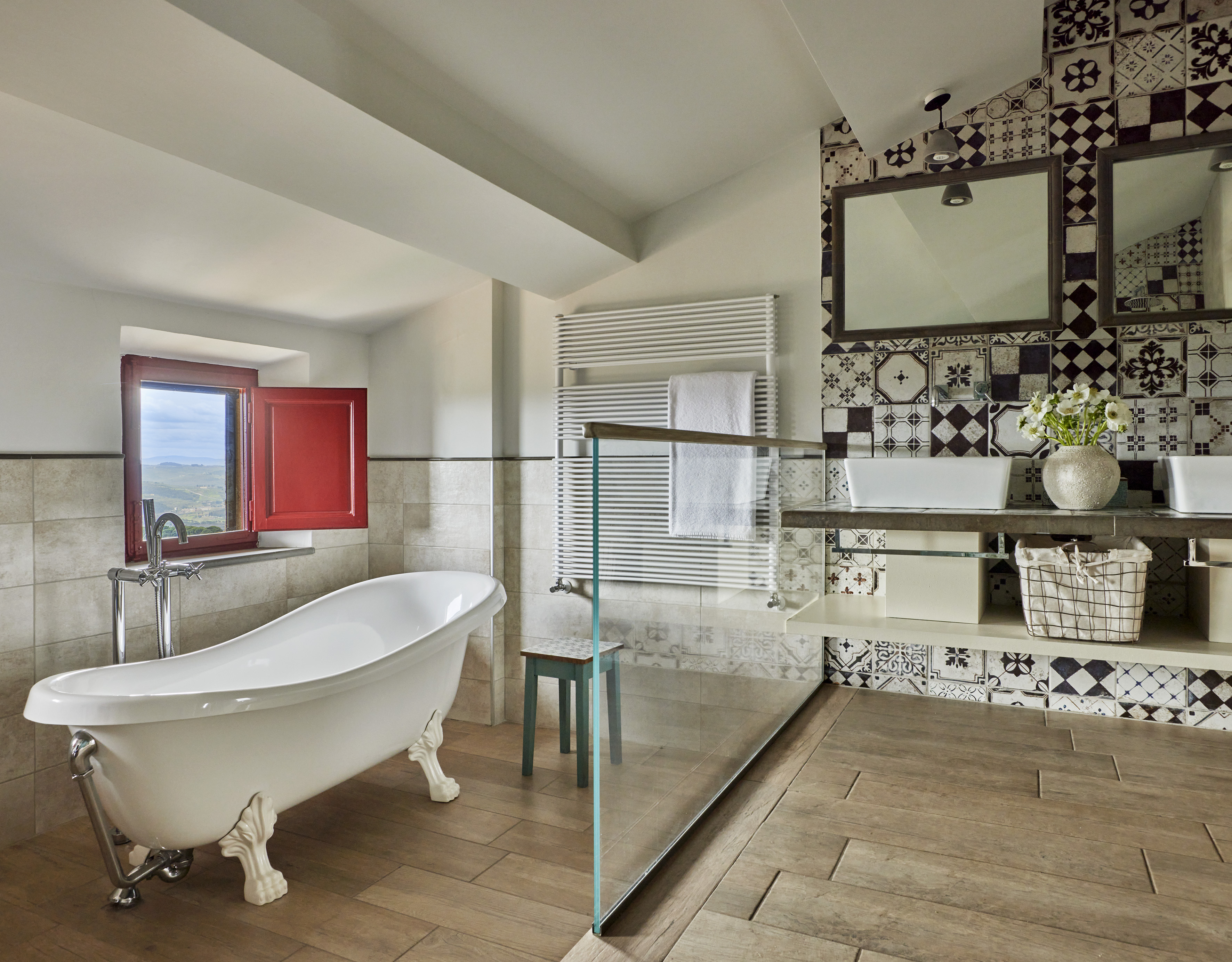 Luxury bathroom with clawfoot tub, red shutters, wood floor, and patterned tiles.