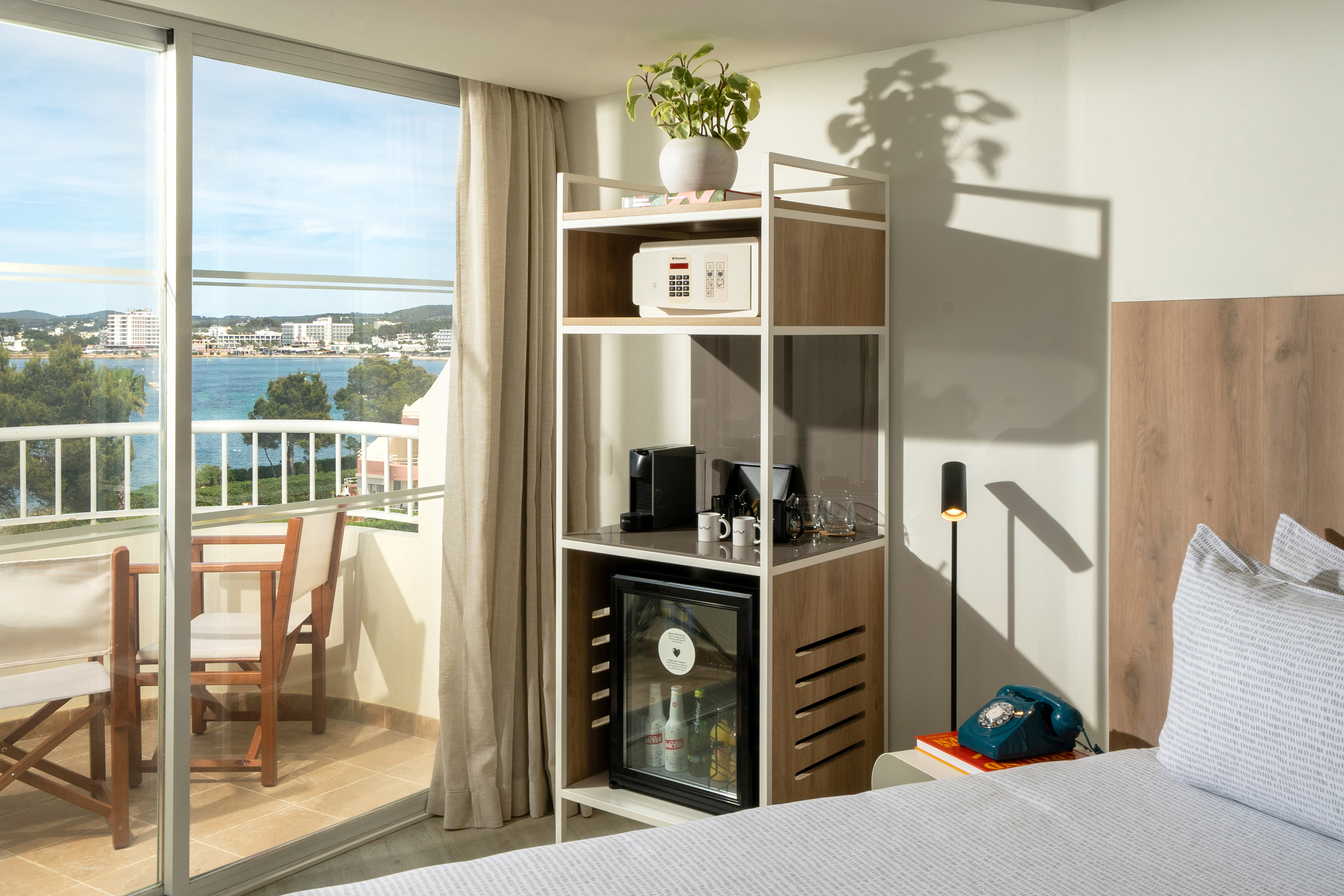 Modern hotel bedroom with ocean view balcony, minibar, safe, and coffee maker.