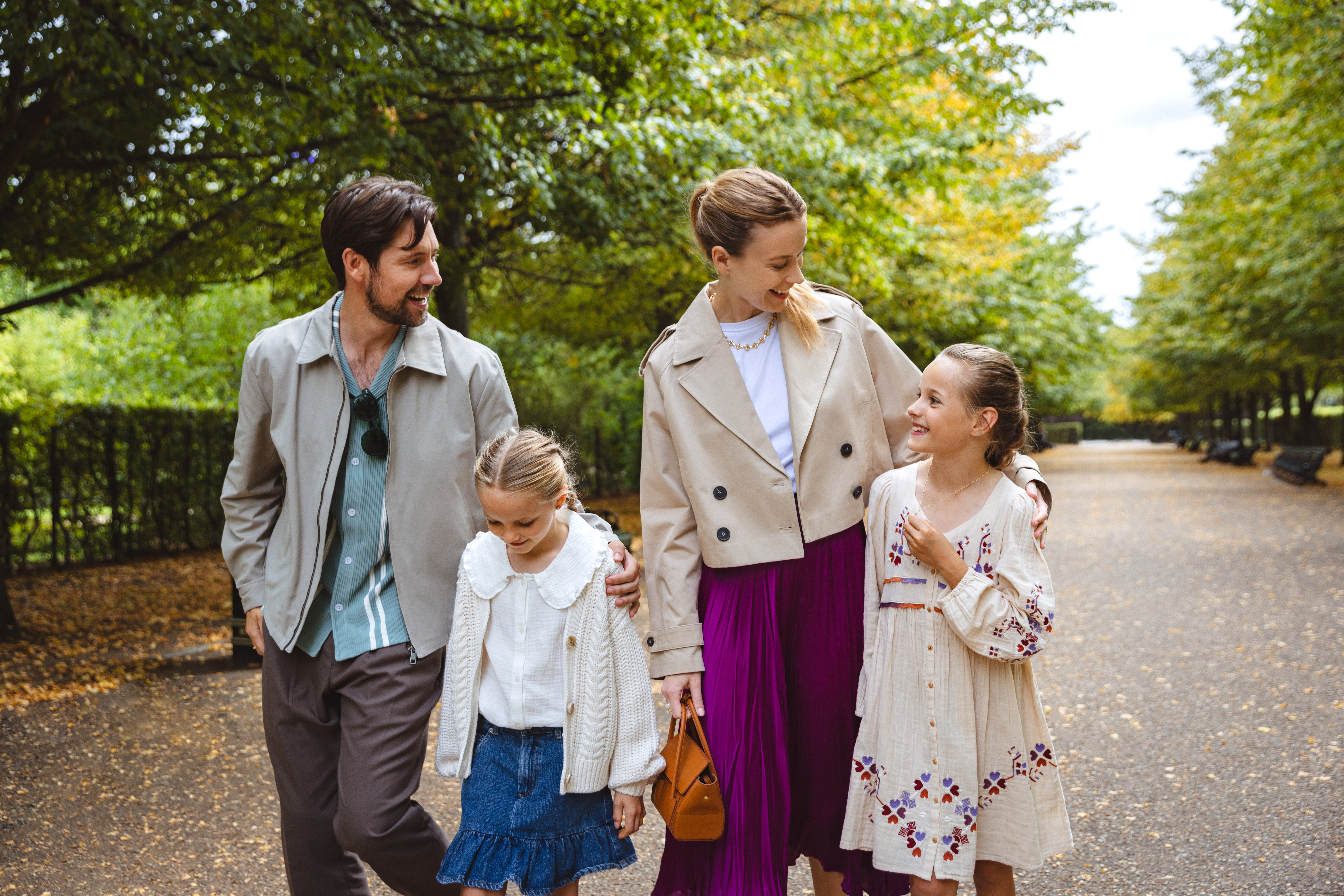 Family with two daughters walking on a tree-lined path, fall season.