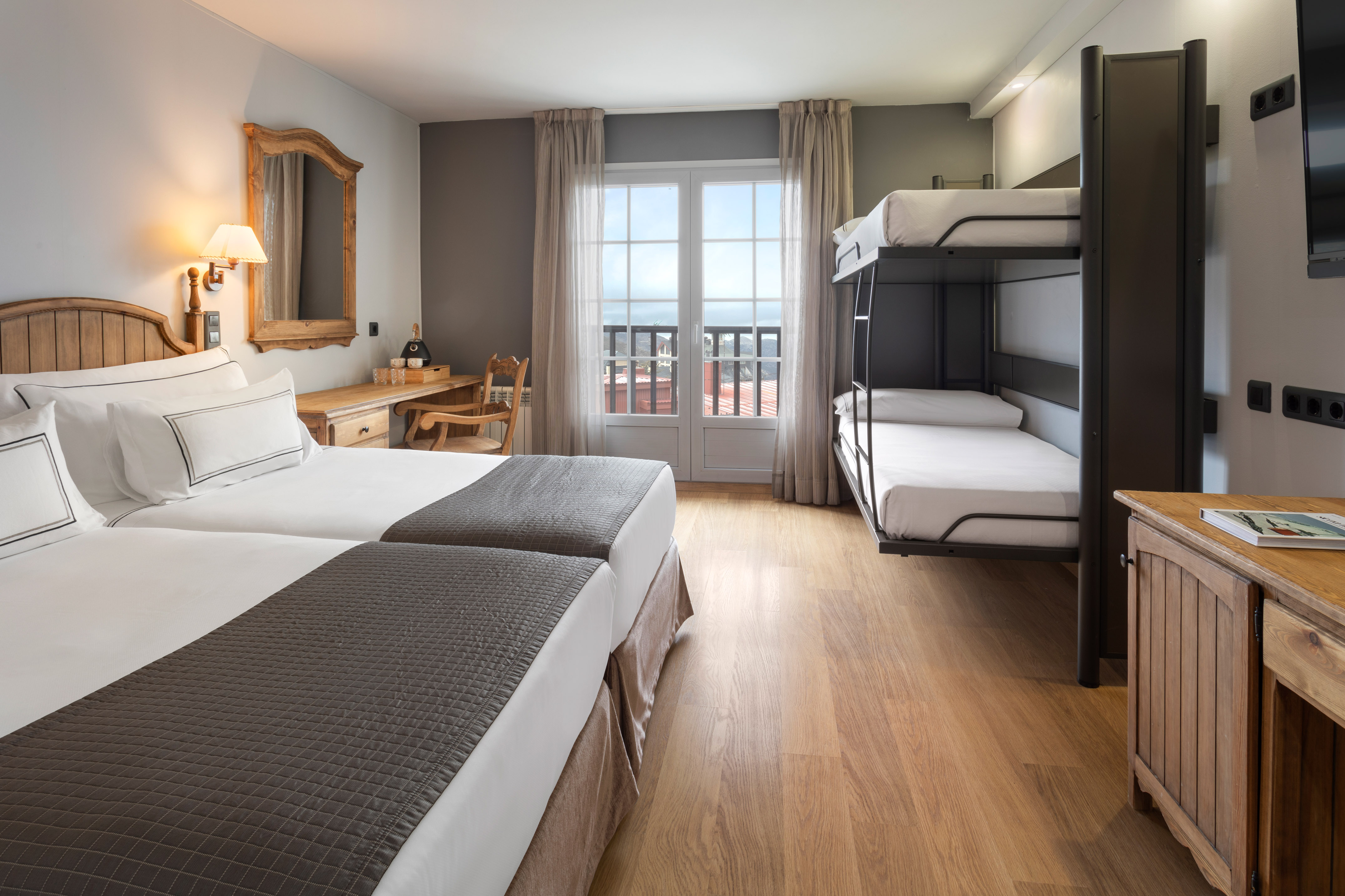 Family hotel room, twin beds, bunk beds, wooden desk, balcony view.