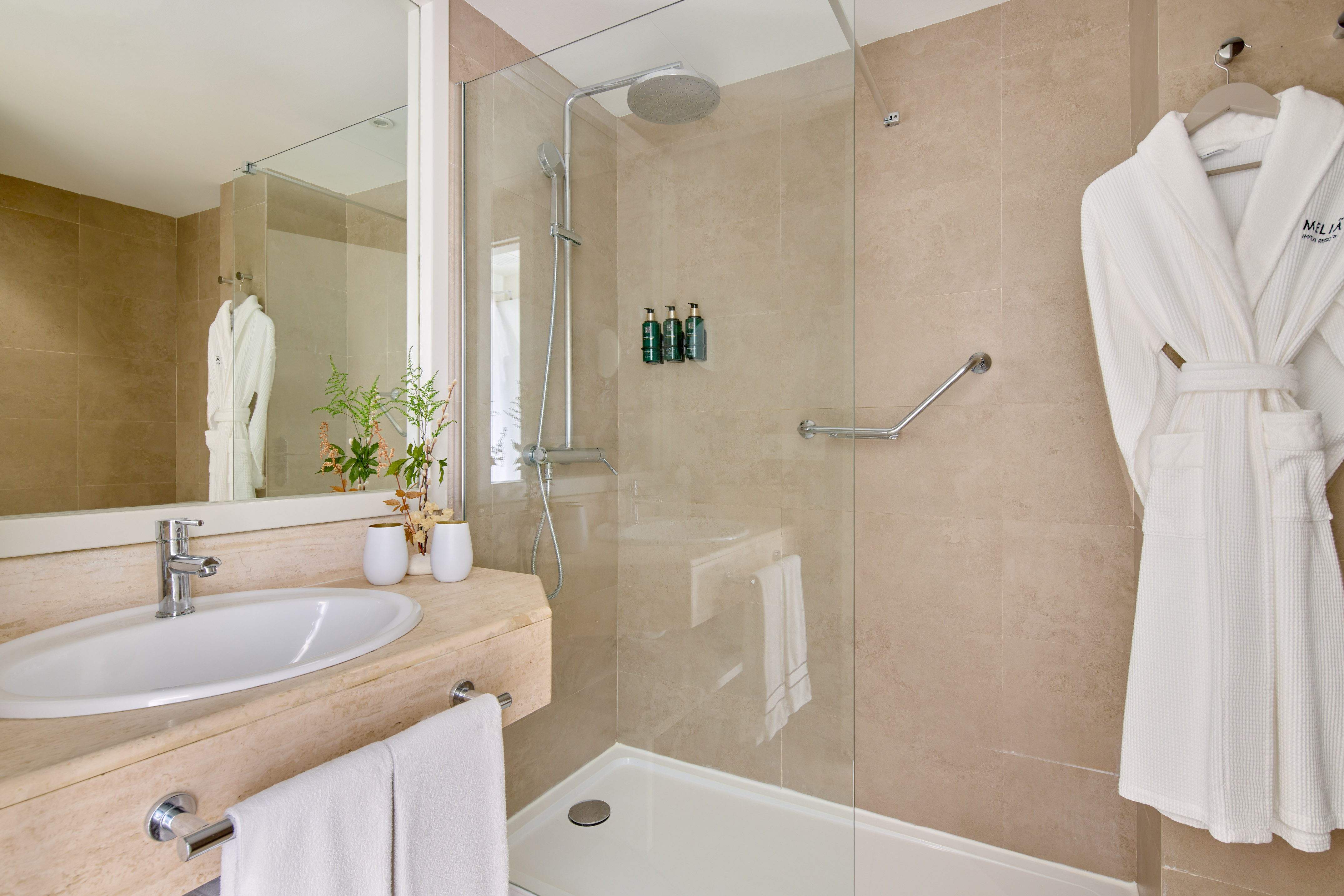 Melia hotel bathroom with modern walk-in shower, vanity, and white bathrobe.