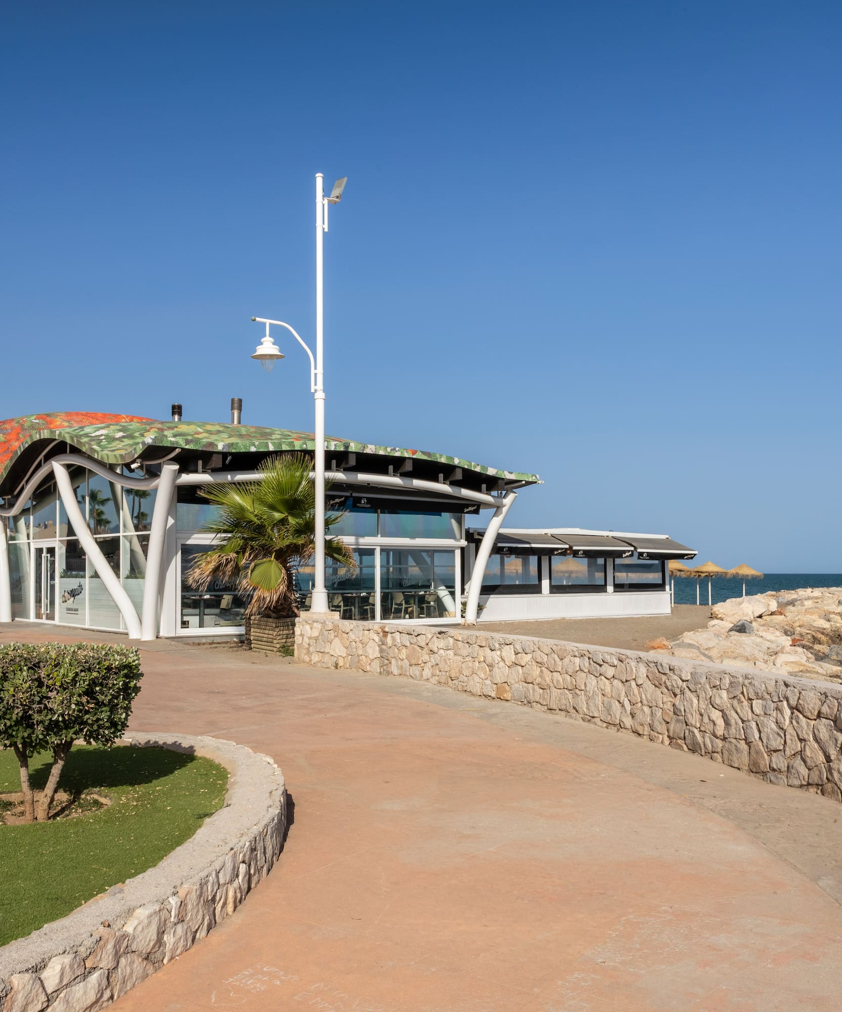 Modern coastal restaurant with unique wavy roof, promenade, and sea view.