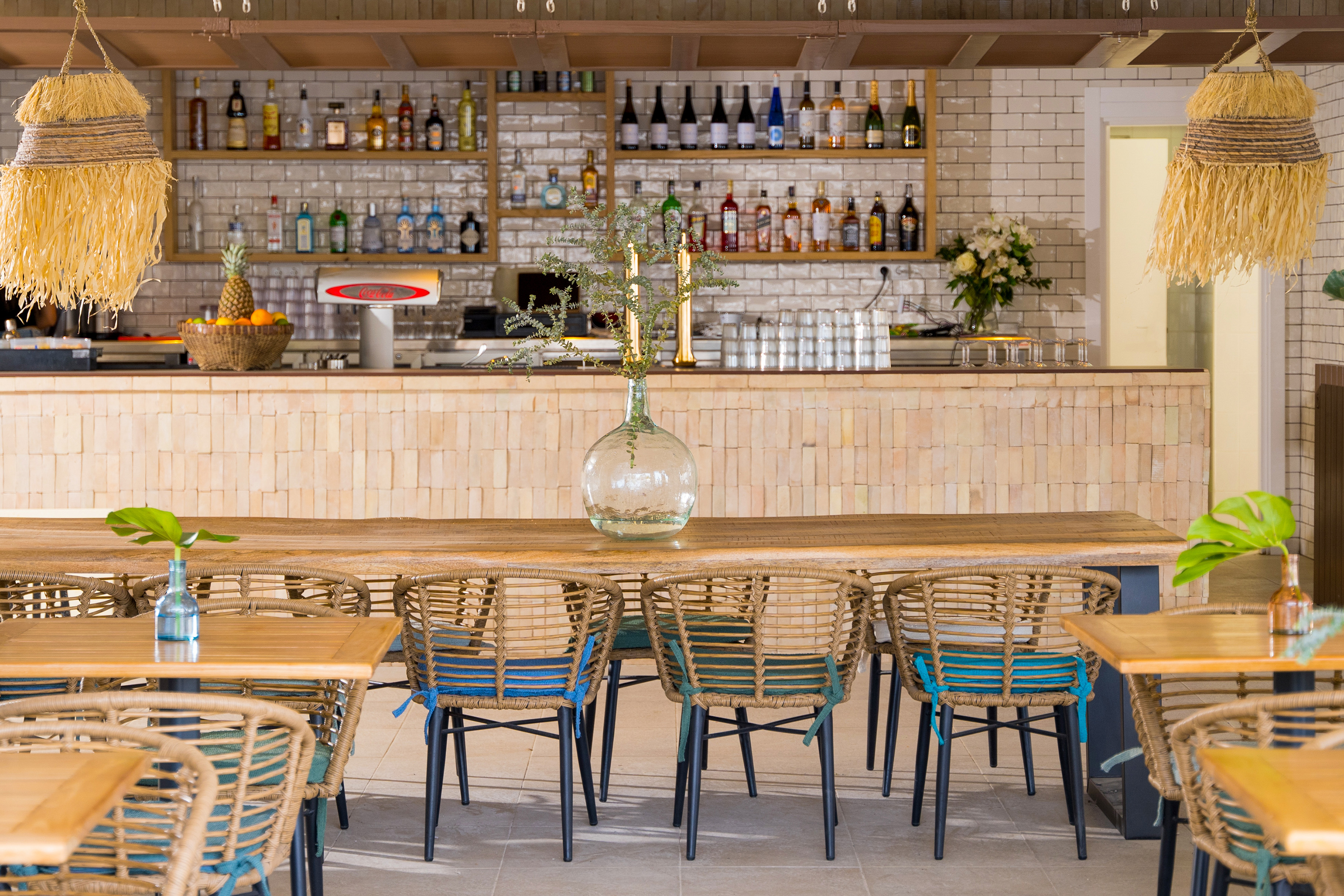 Bohemian resort bar with rattan chairs, wooden table, and tropical decor.