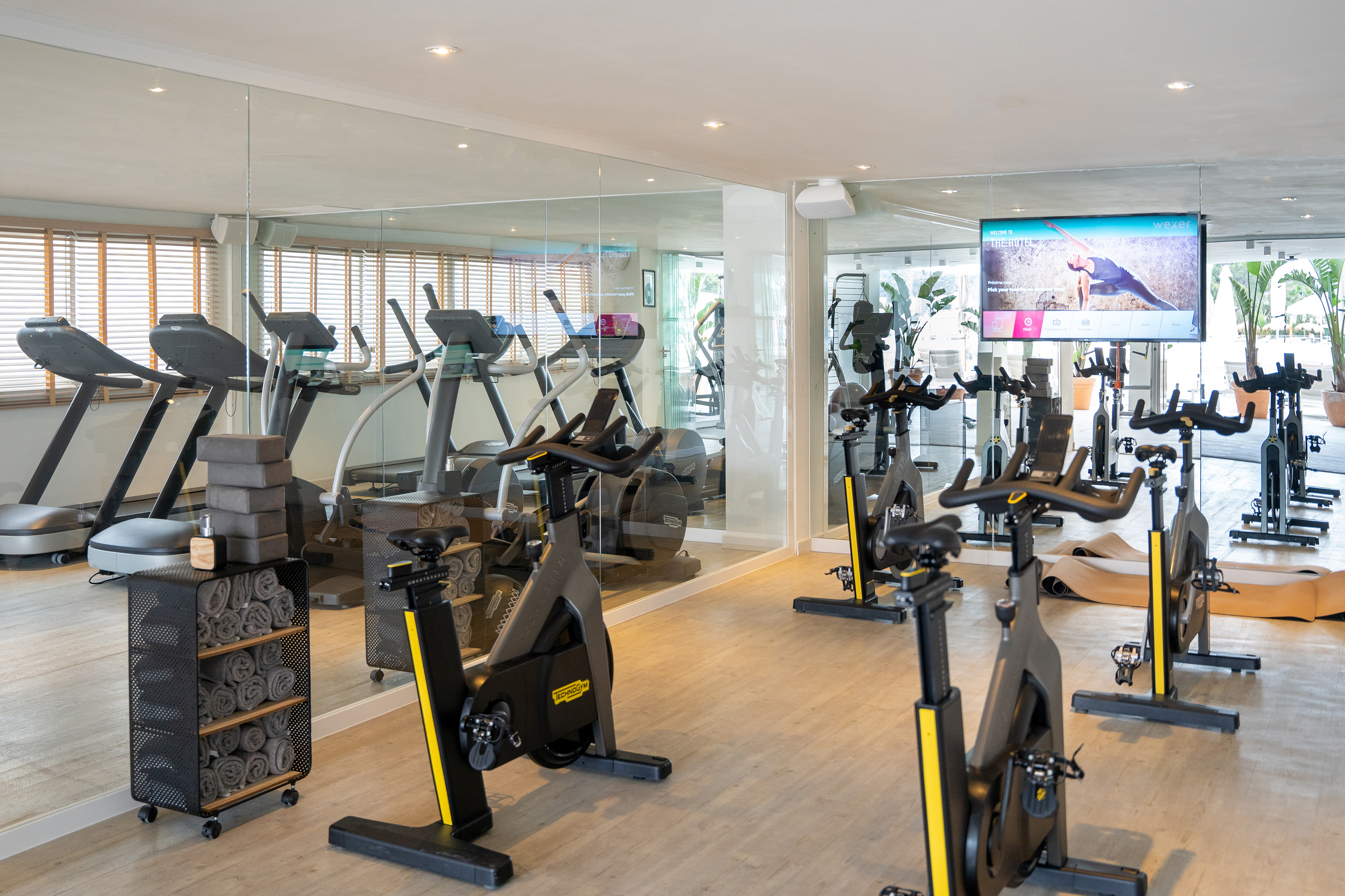 Hotel gym with spin bikes, treadmills, mirrored walls, and a large workout screen.