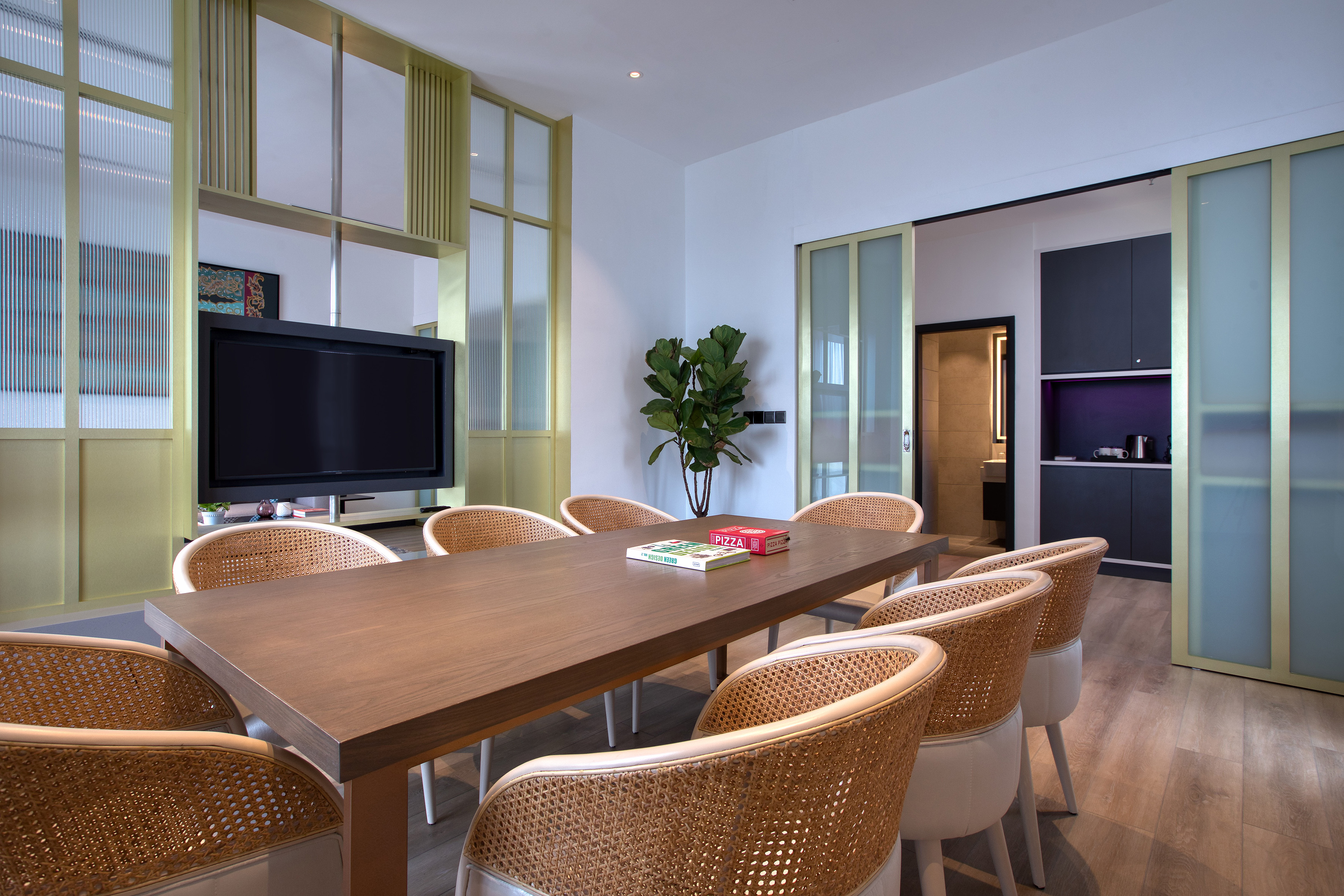 Modern dining area with long wooden table, rattan chairs, TV, and gold partitions.