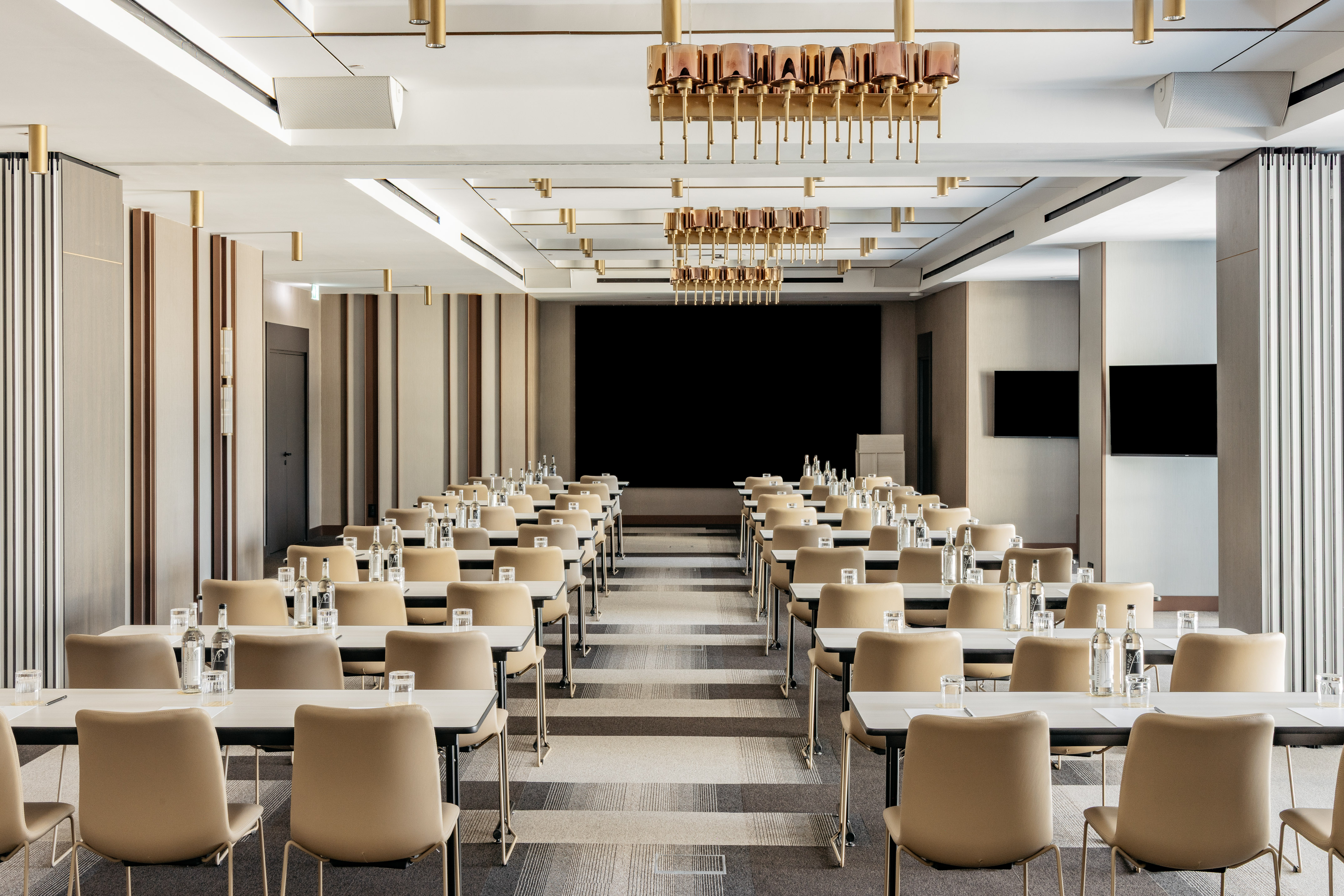Spacious meeting room with classroom setup, large screen, and modern decor.