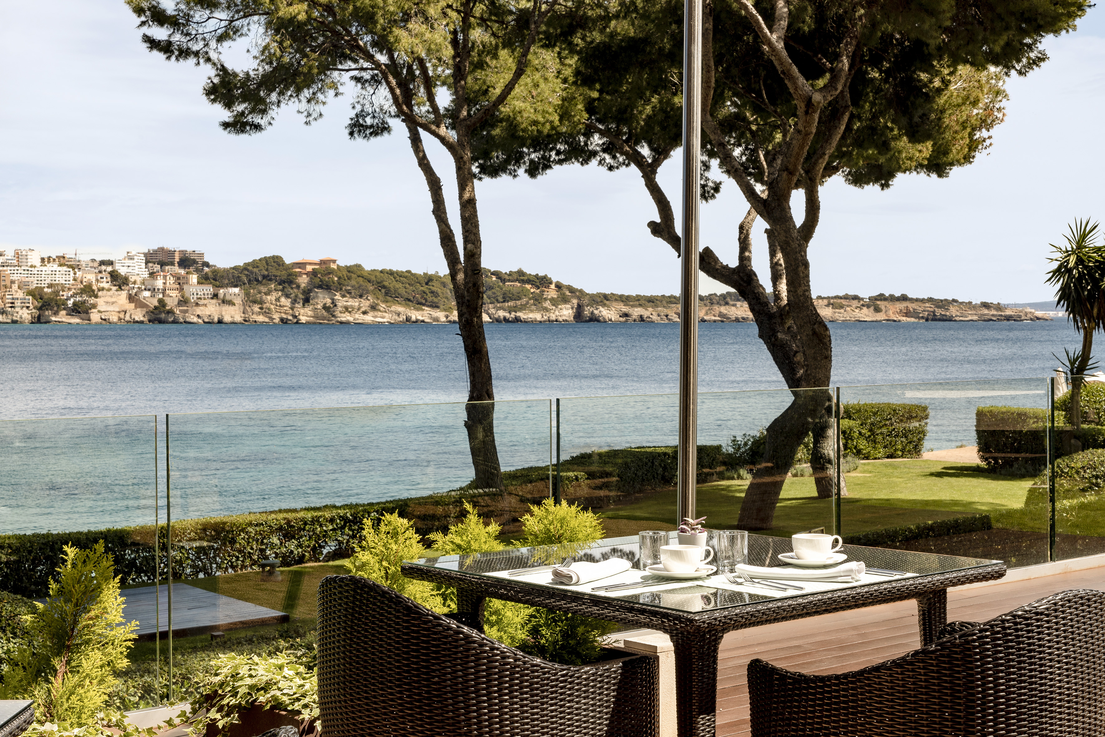 Outdoor restaurant table set with sea view, lush garden, and coastal town.