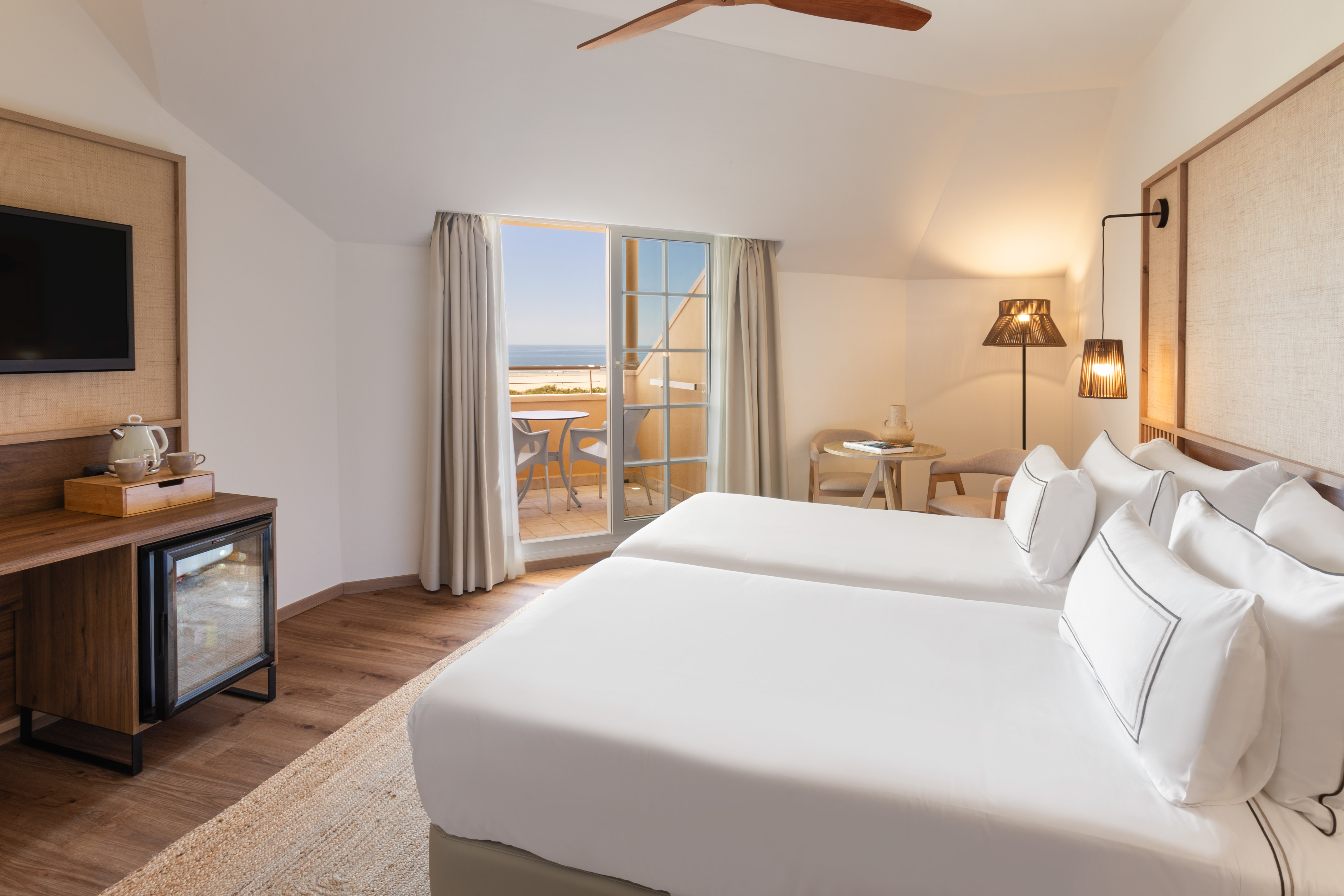 Bright hotel room with twin beds, private balcony, and ocean view.