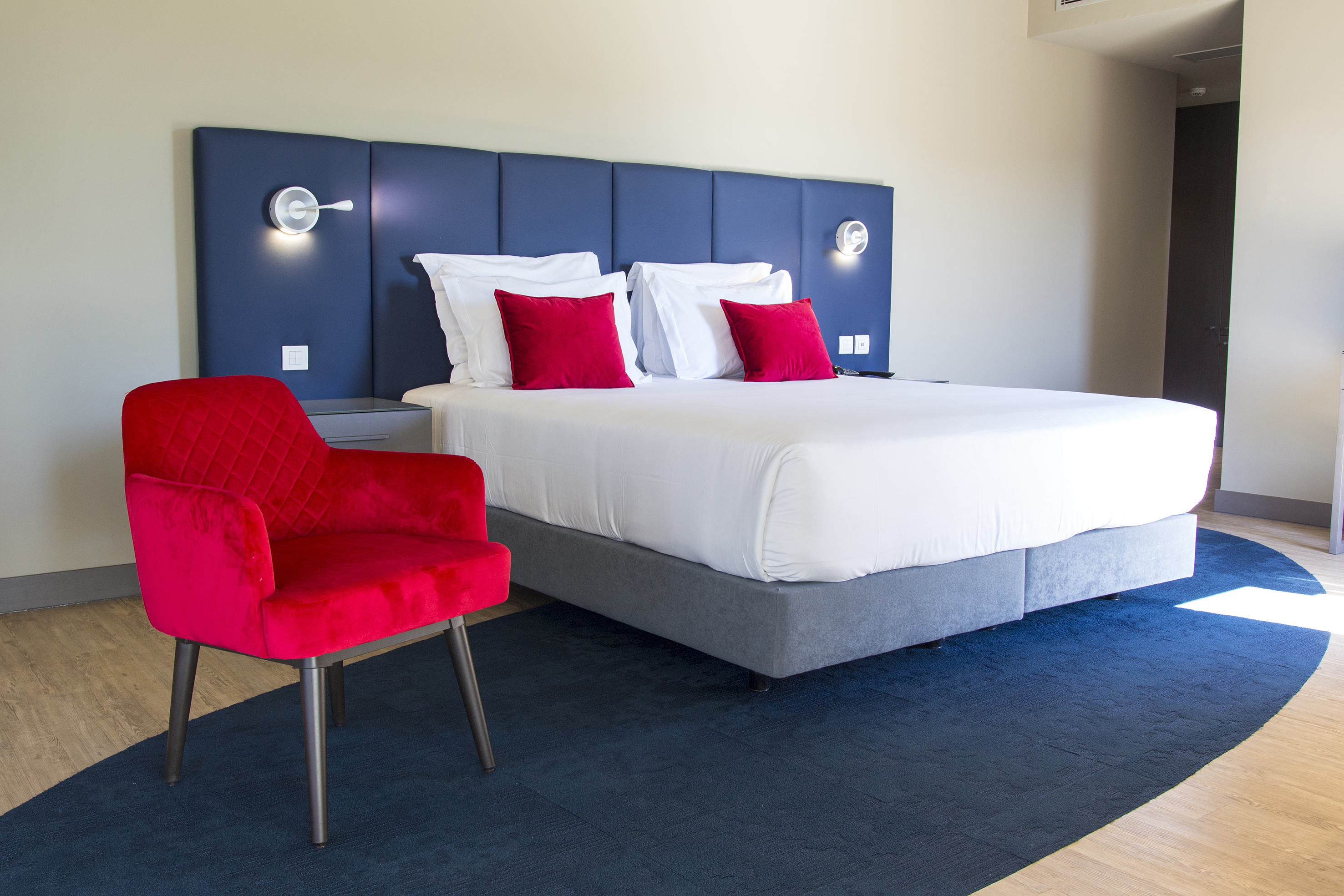 Modern bedroom with king bed, blue headboard, and red velvet armchair.