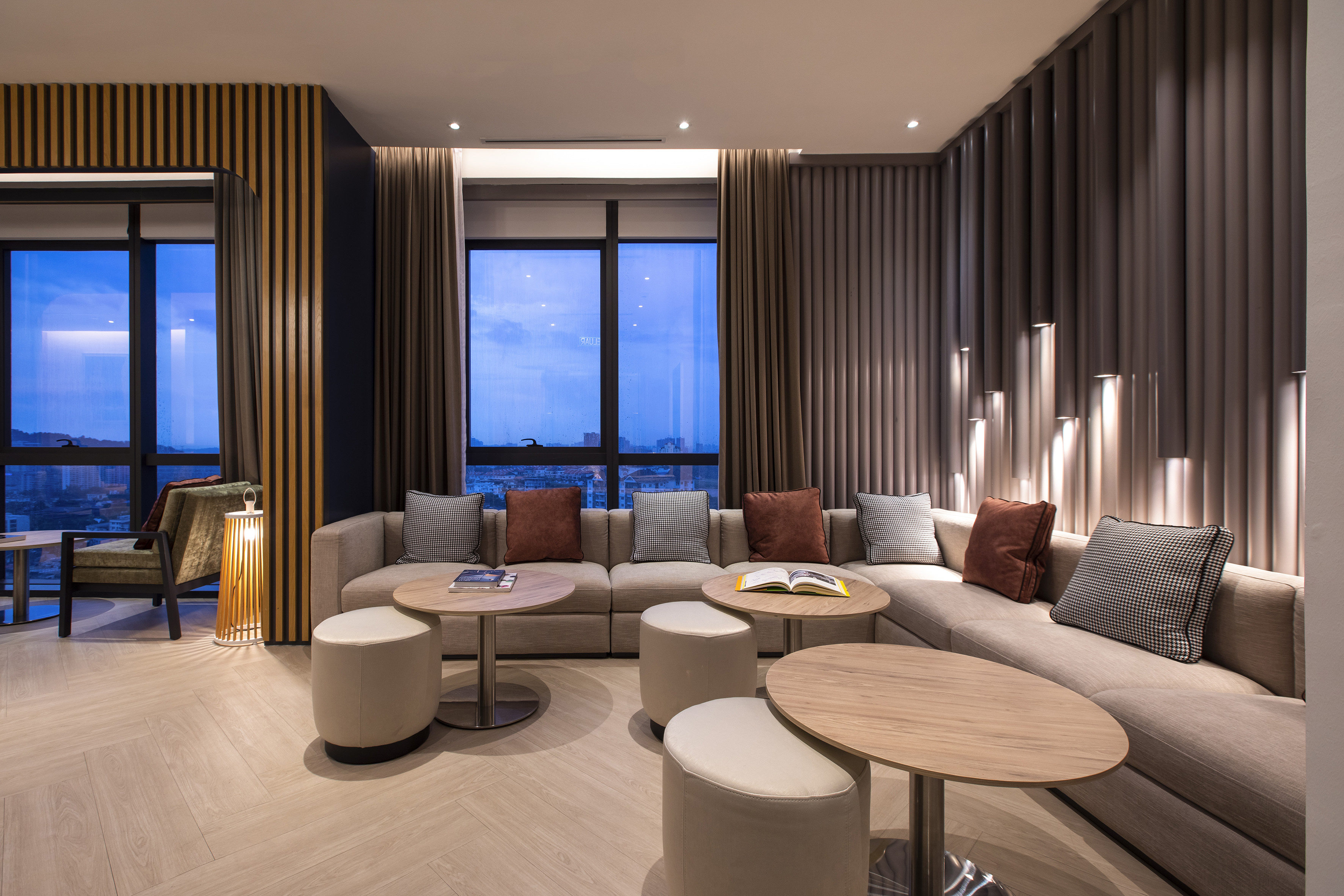 Modern lounge with beige sectional sofa, city view, and elegant accent walls.