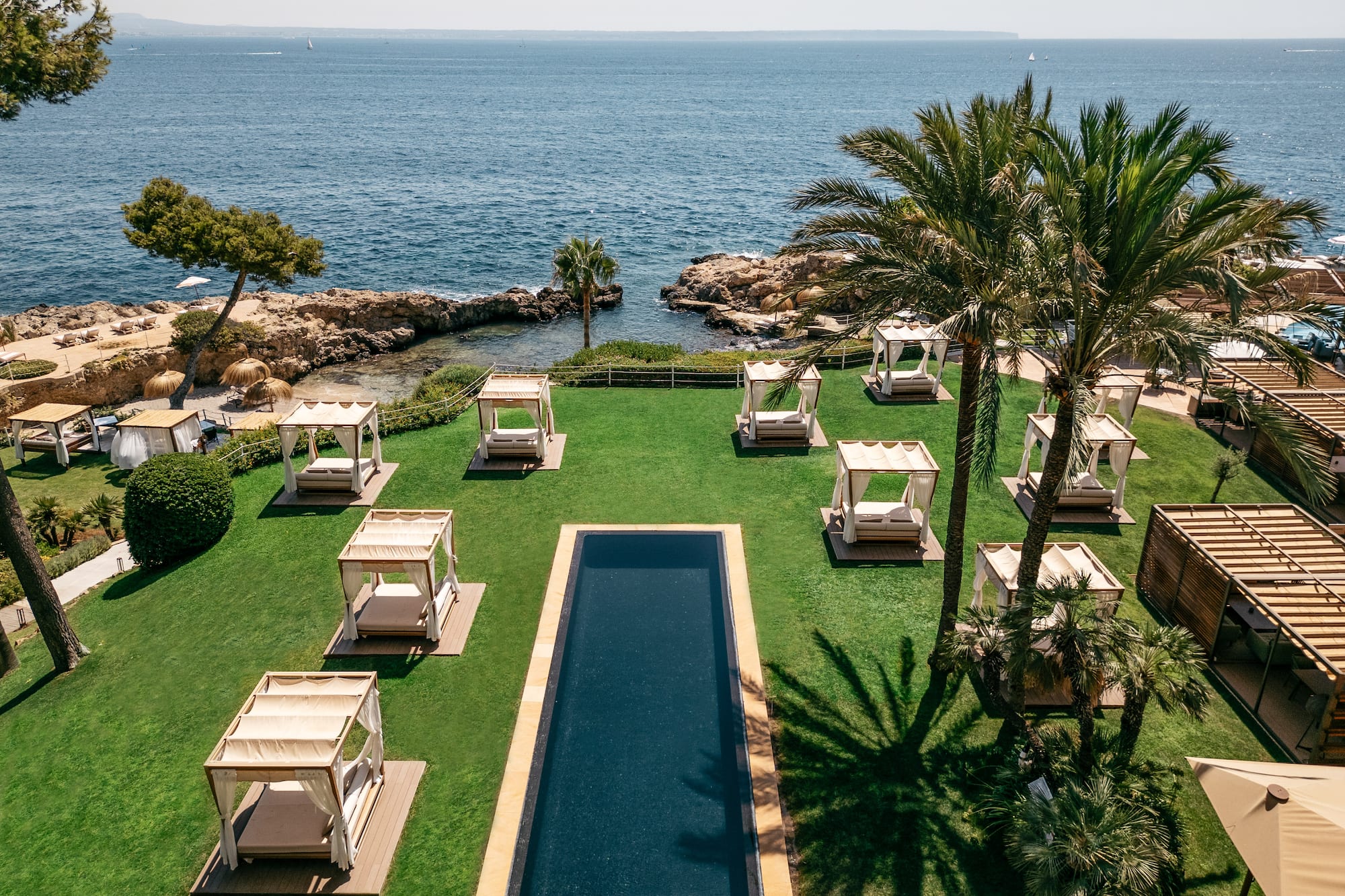 Coastal resort garden with pool, cabanas, palm trees, and ocean view.