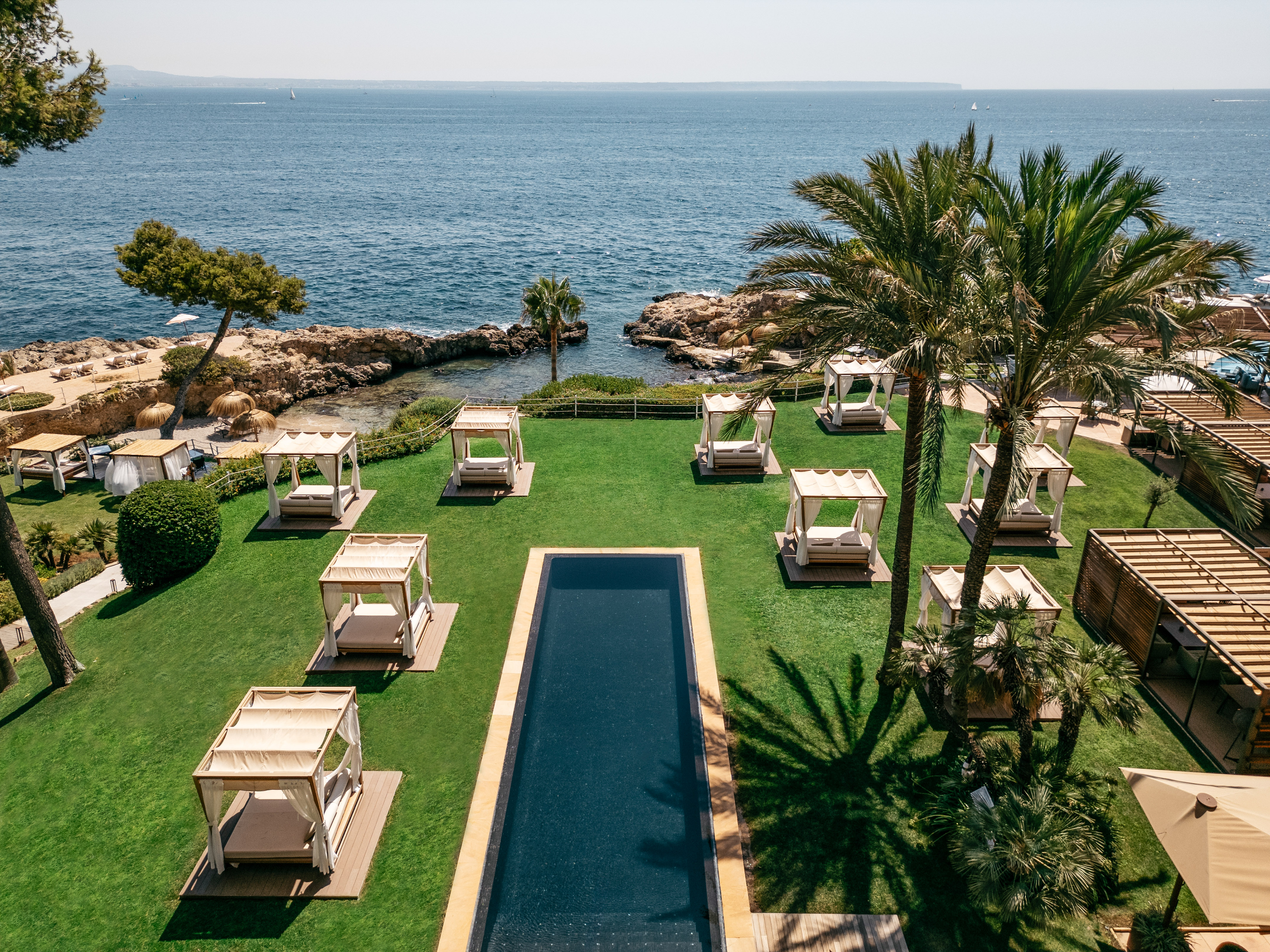 Coastal resort garden with pool, cabanas, palm trees, and ocean view.