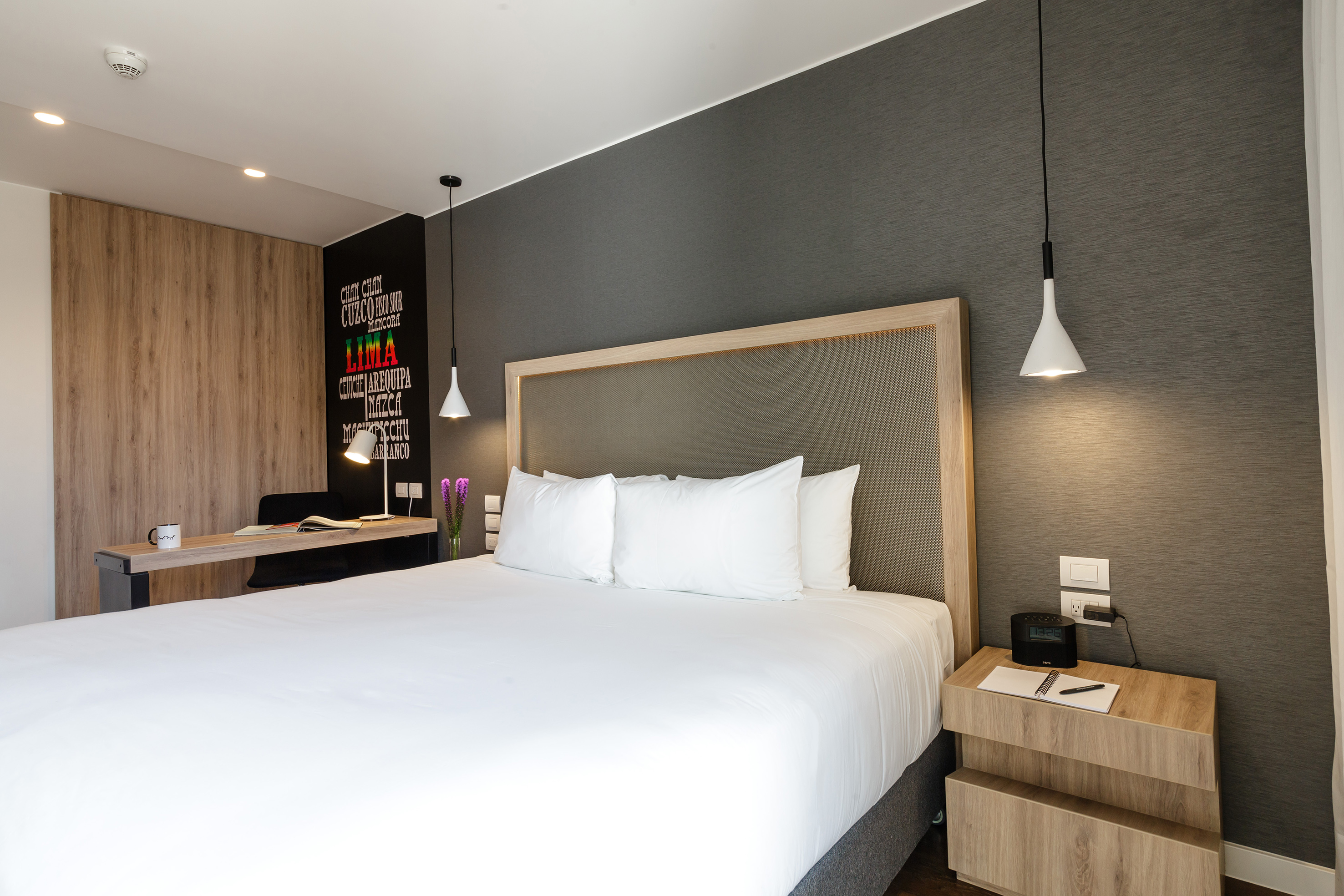 Modern hotel room with bed, wooden desk, and Peruvian destination wall.