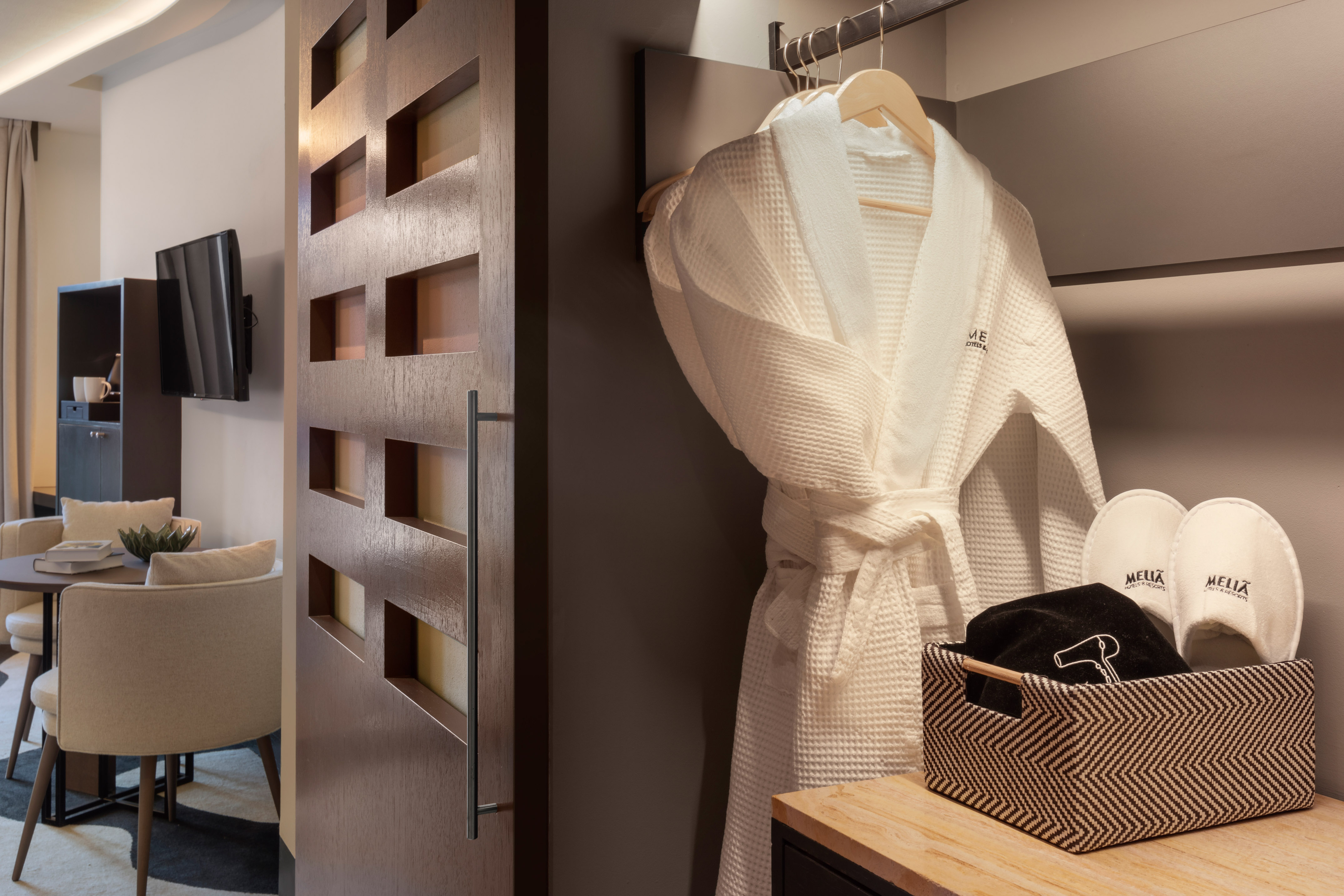 White Meliá hotel bathrobe and slippers in modern room closet with amenities.