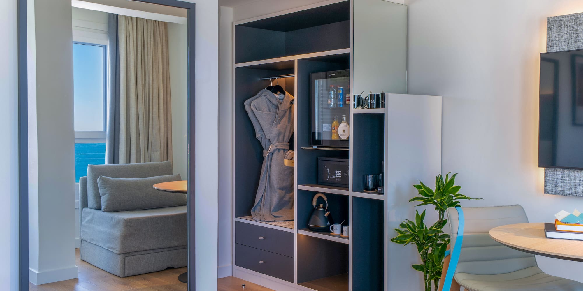 Habitación de hotel: armario, minibar y espejo reflejando vista al mar.