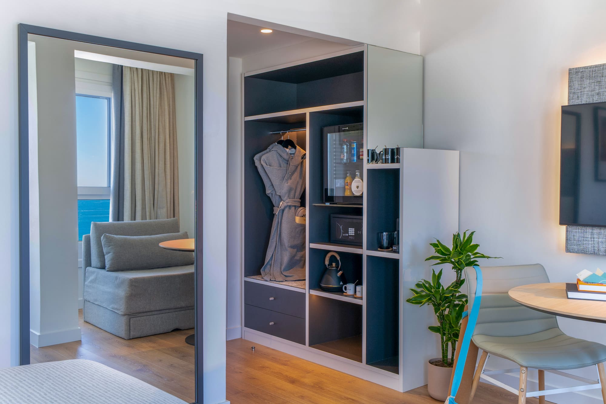 Habitación de hotel: armario, minibar y espejo reflejando vista al mar.