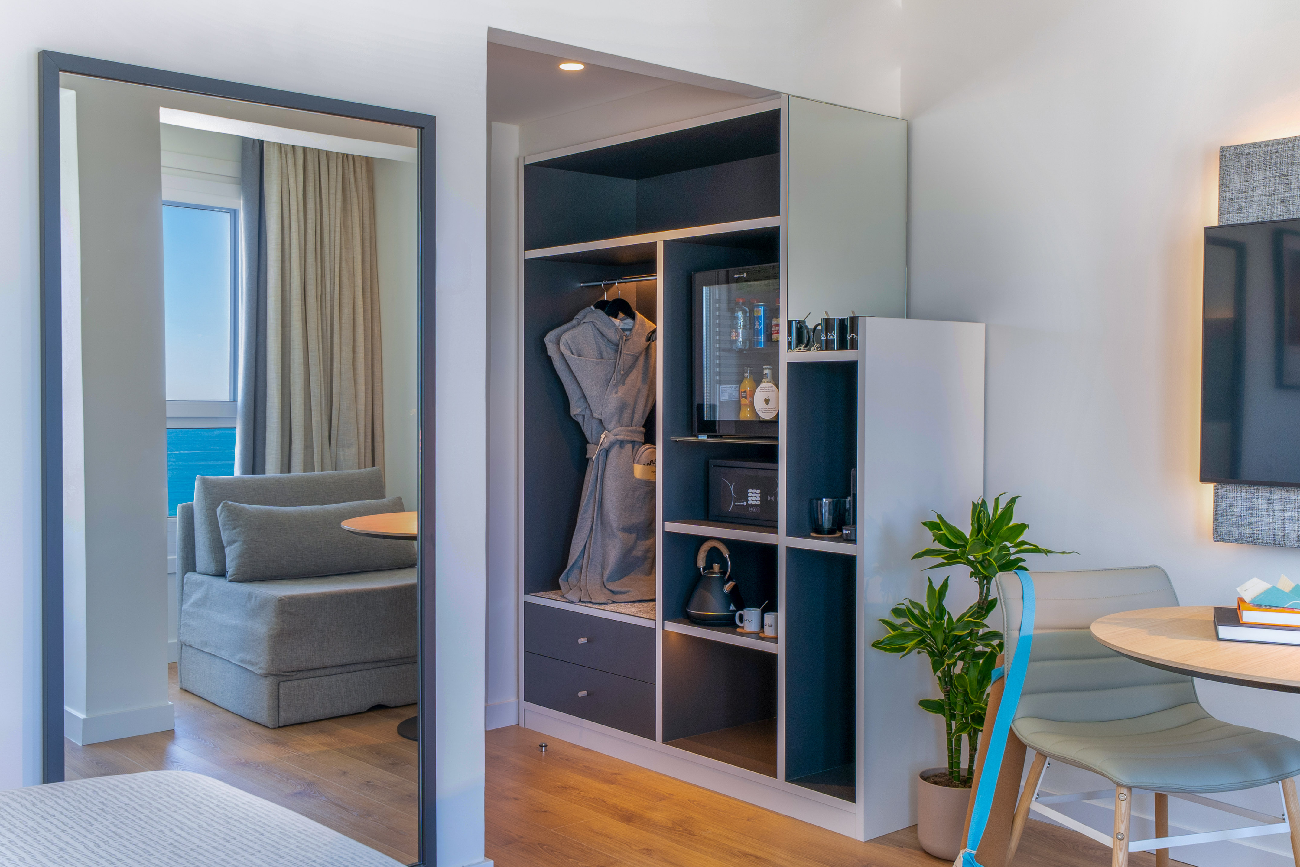 Habitación de hotel: armario, minibar y espejo reflejando vista al mar.
