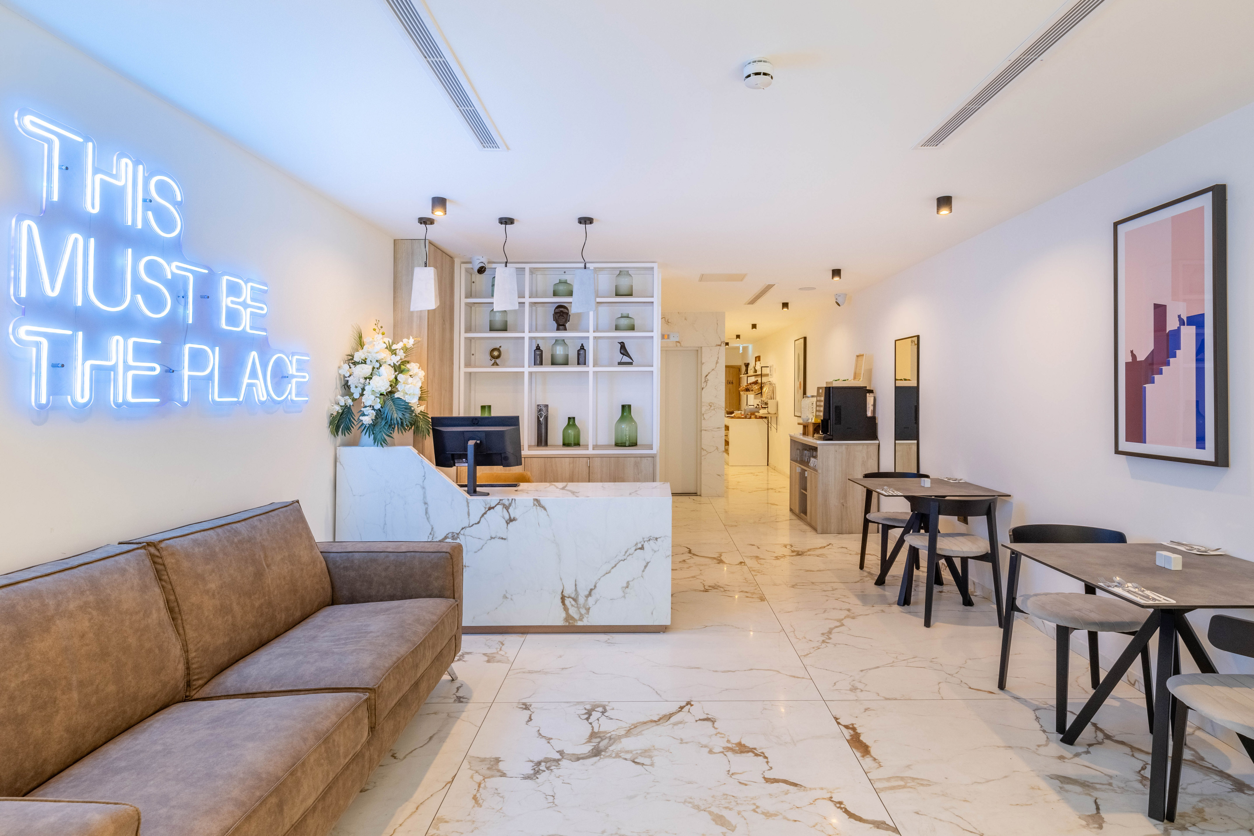 Modern hotel reception & cafe with 'THIS MUST BE THE PLACE' neon sign.