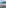 Beach restaurant tables, straw umbrellas, ocean with boats, island background.