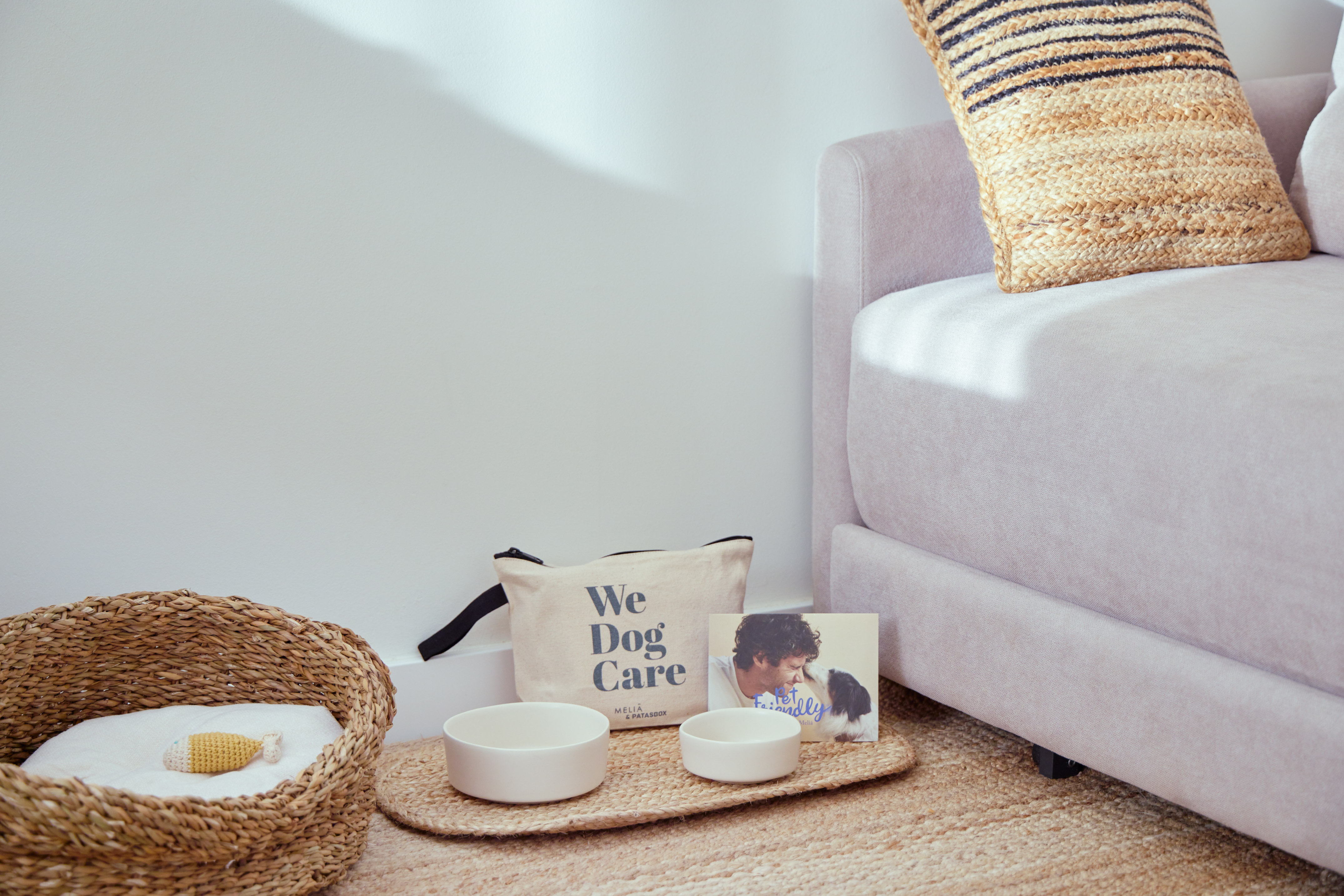 Pet-friendly room with woven dog bed, white bowls, "We Dog Care" bag.