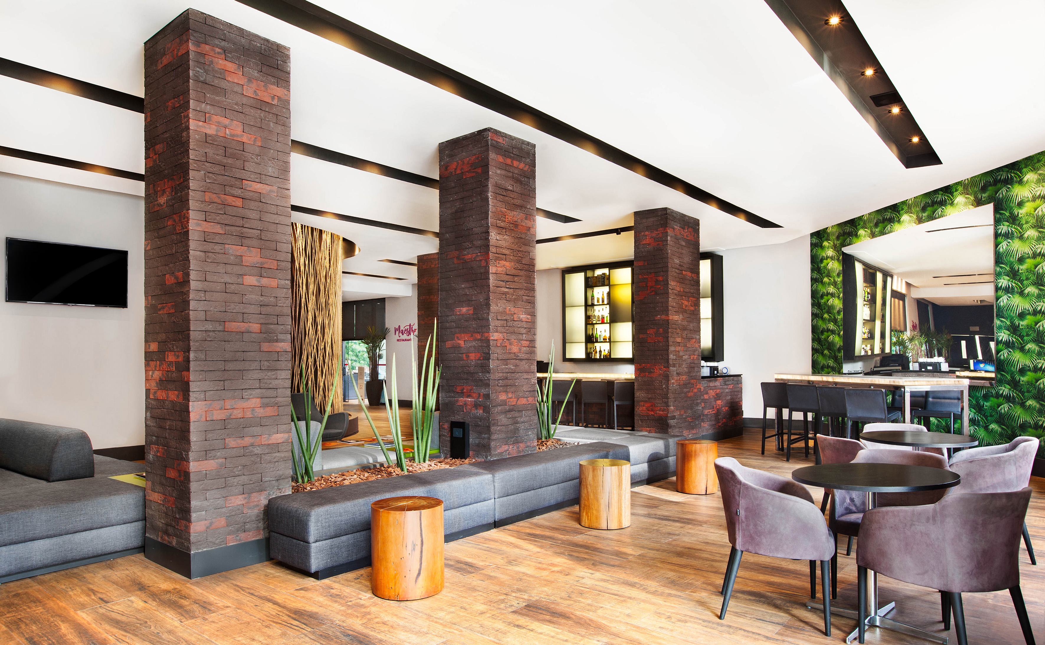 Hotel lobby bar with brick columns, modern seating, and green wall decor.