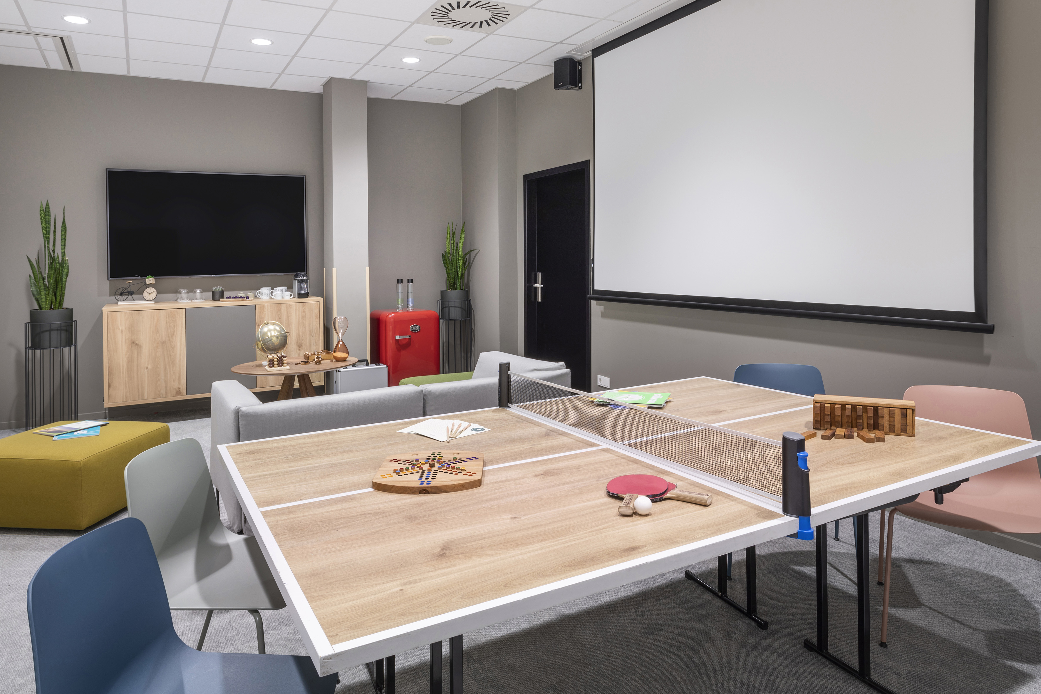 Modern game room with ping pong table, board games, TV, and projector screen.