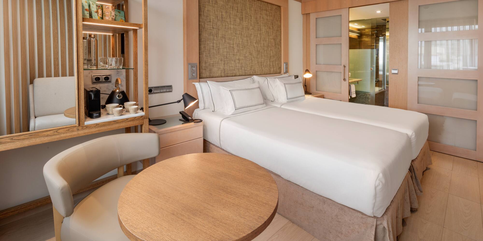 Modern hotel room with twin beds, coffee station, and wood paneling.