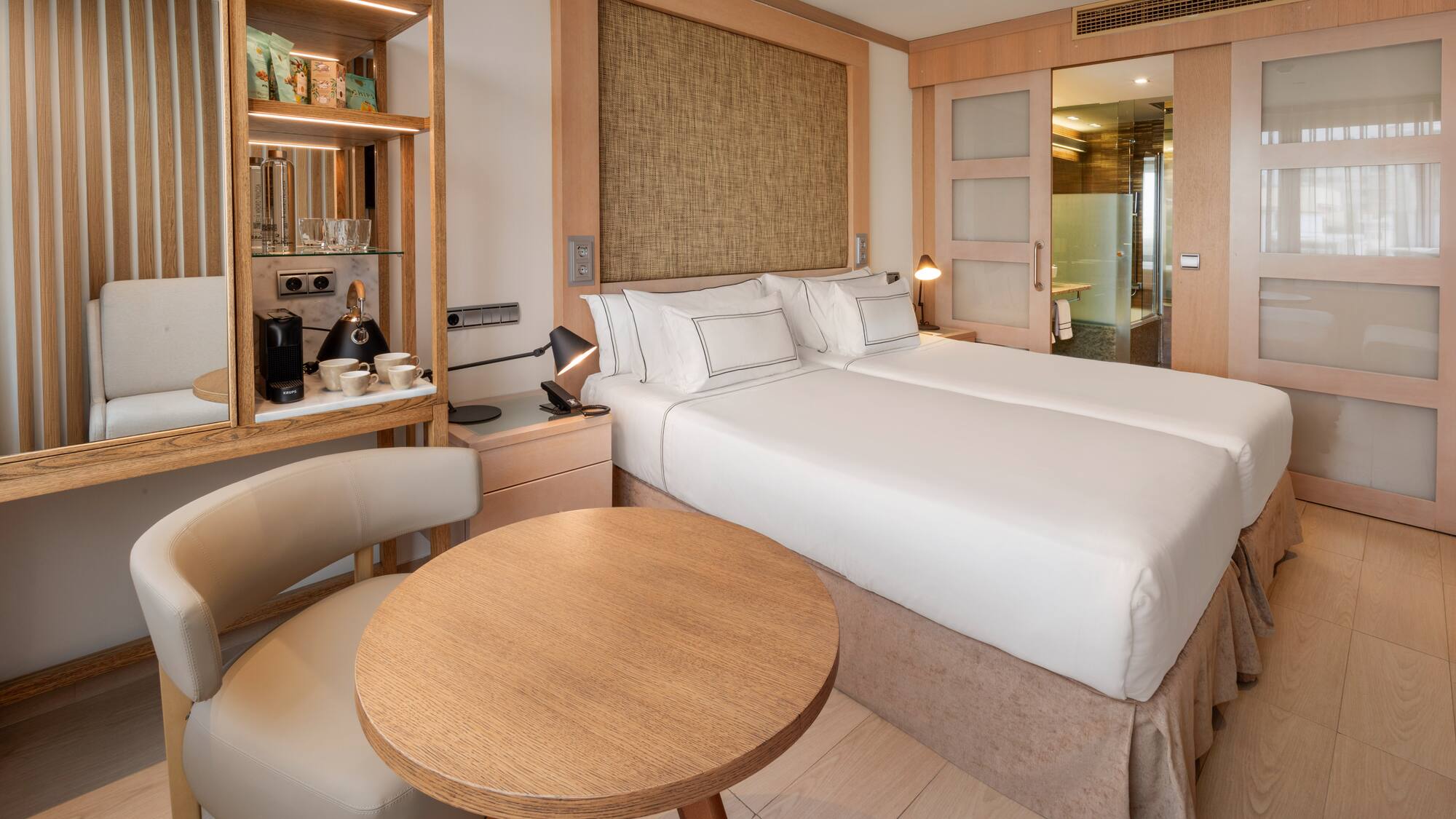 Modern hotel room with twin beds, coffee station, and wood paneling.