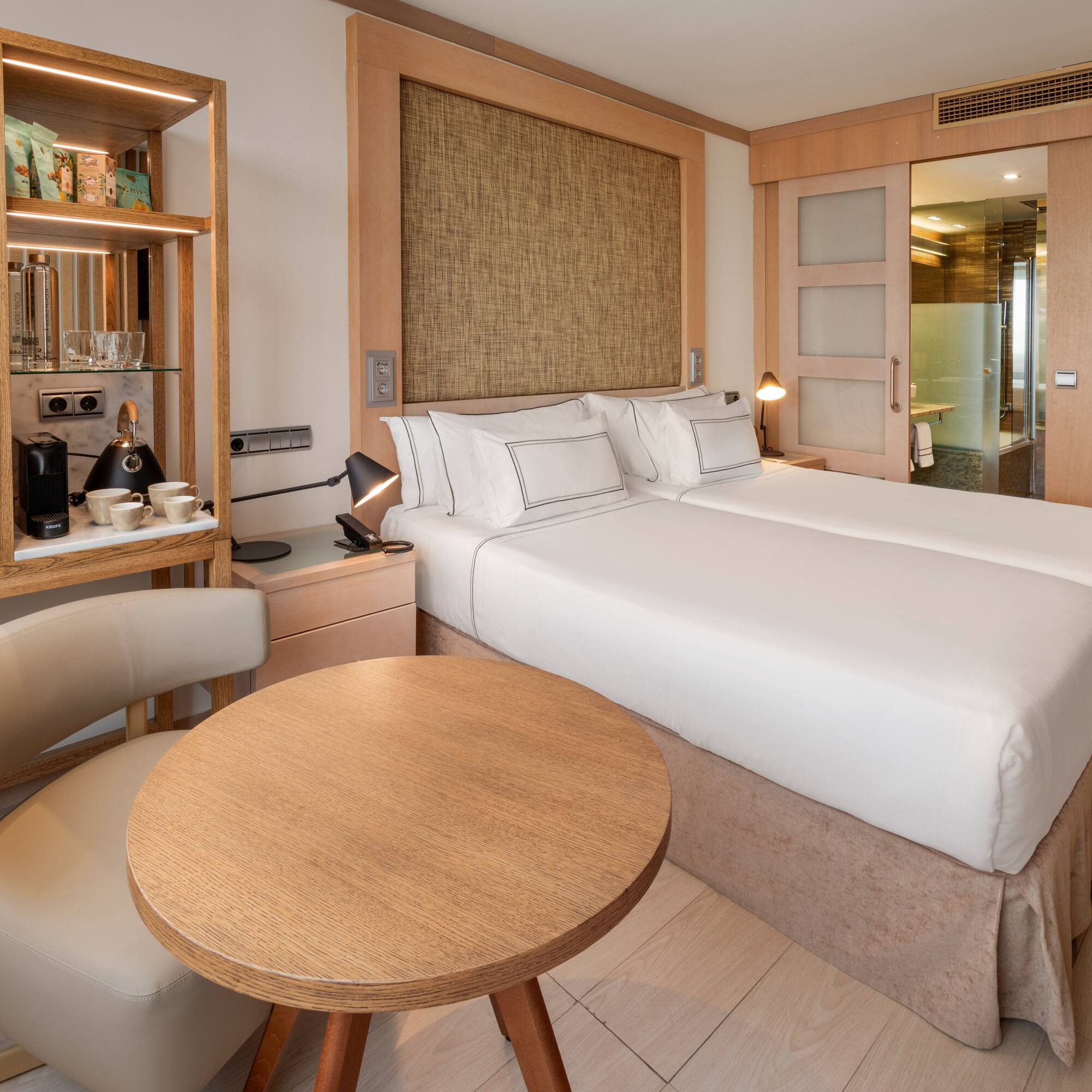 Modern hotel room with twin beds, coffee station, and wood paneling.