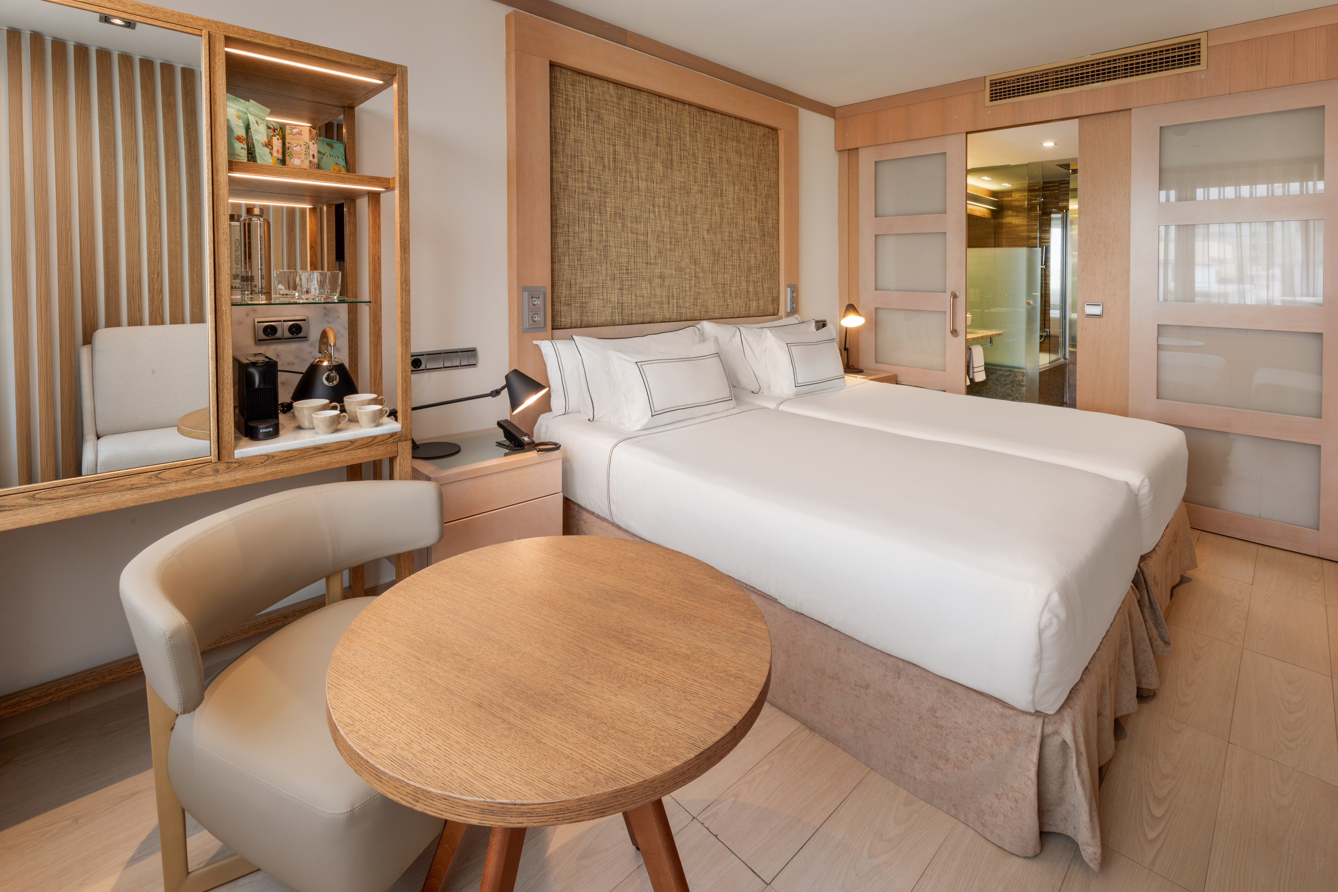 Modern hotel room with twin beds, coffee station, and wood paneling.