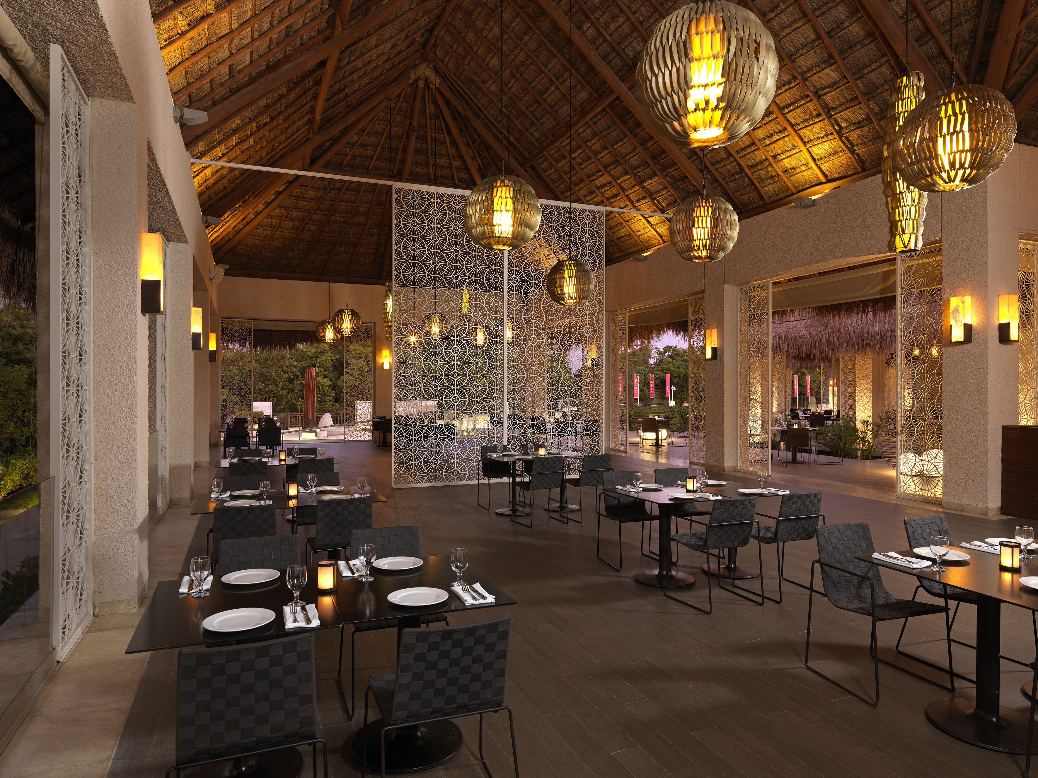 Elegant resort restaurant with thatched roof, warm lighting, and set tables.