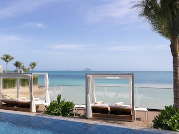 a pool with lounge chairs and a beach in the background