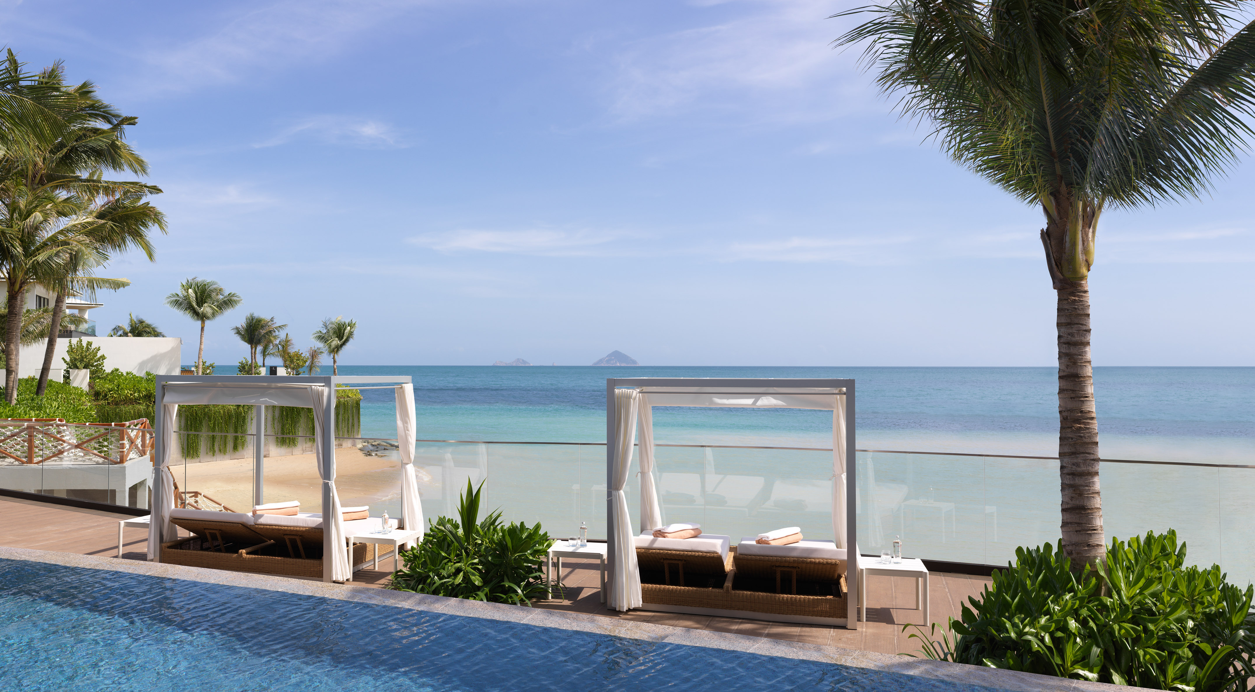 Tropical beach resort with poolside cabanas, ocean, and palm trees.