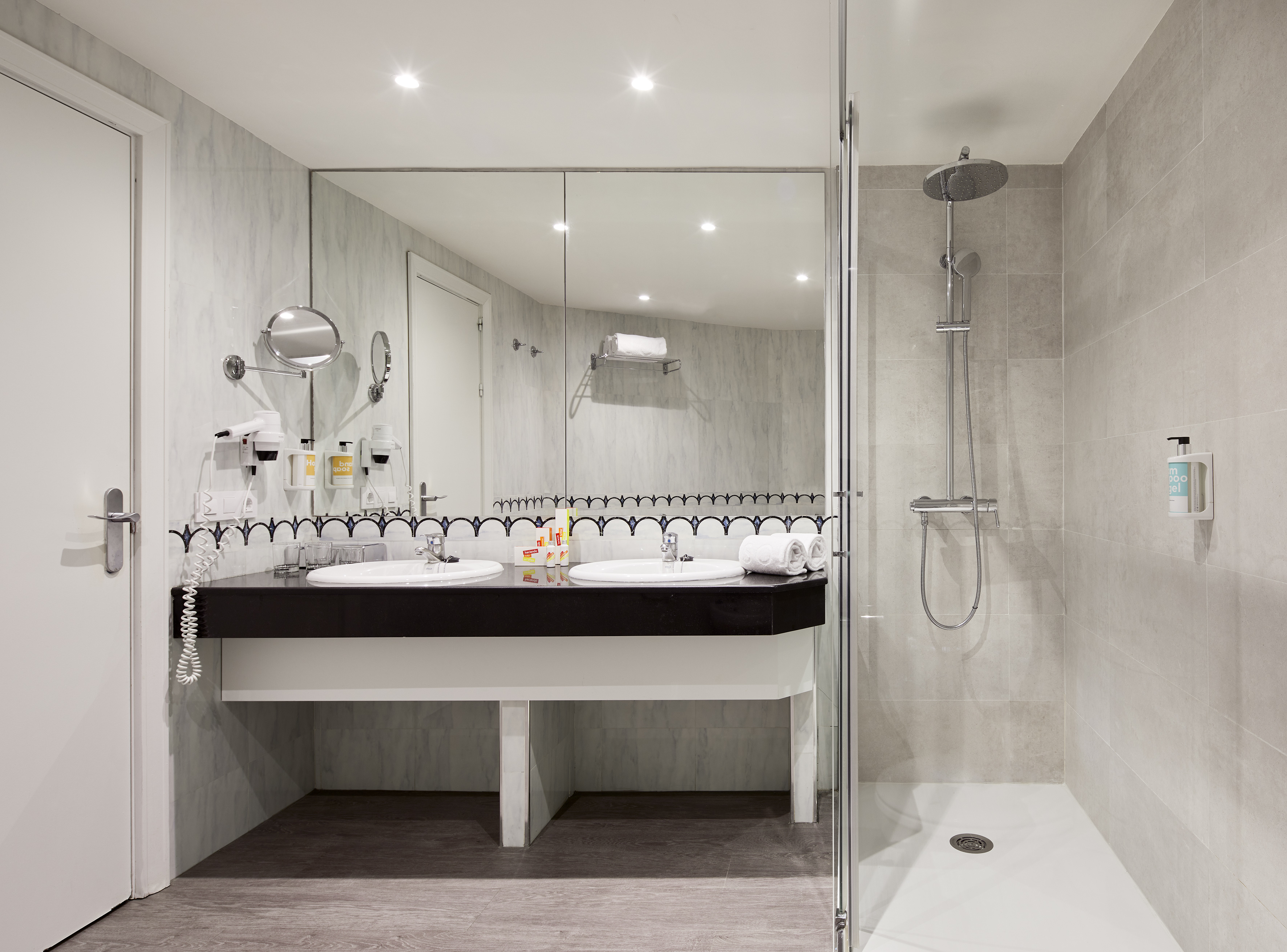 Contemporary hotel bathroom with double vanity, large mirror, and glass shower.