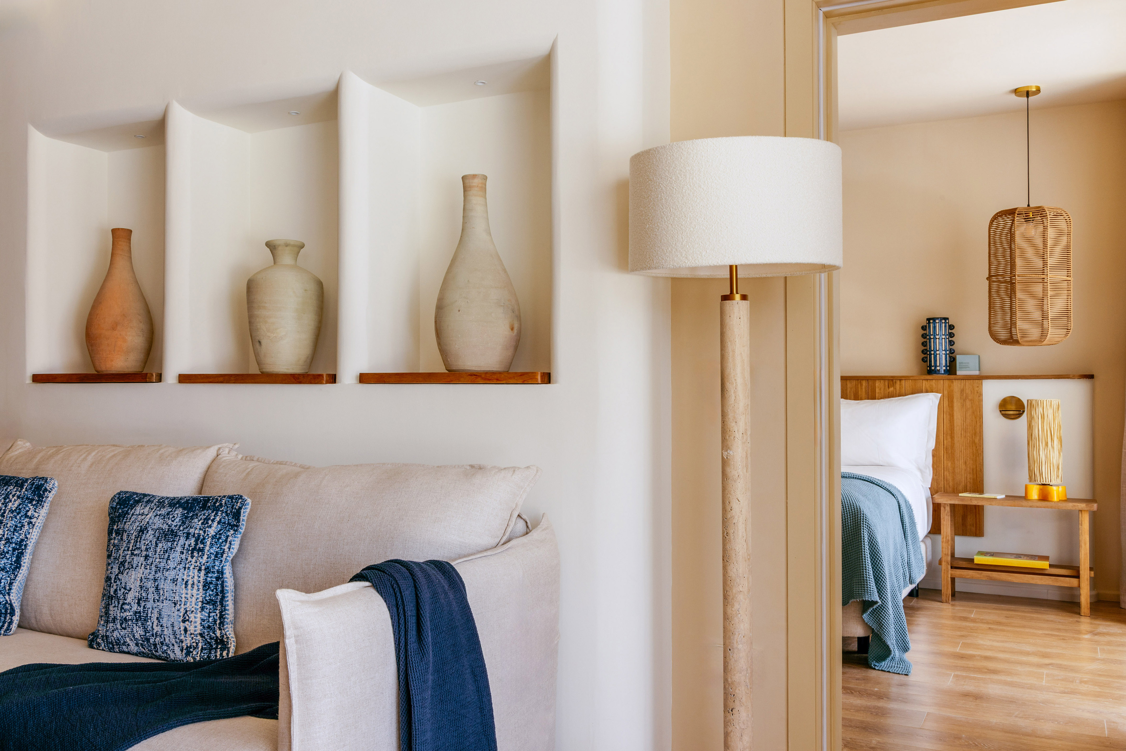 Boho style living room with sofa, ceramic vases, floor lamp, and bedroom view.