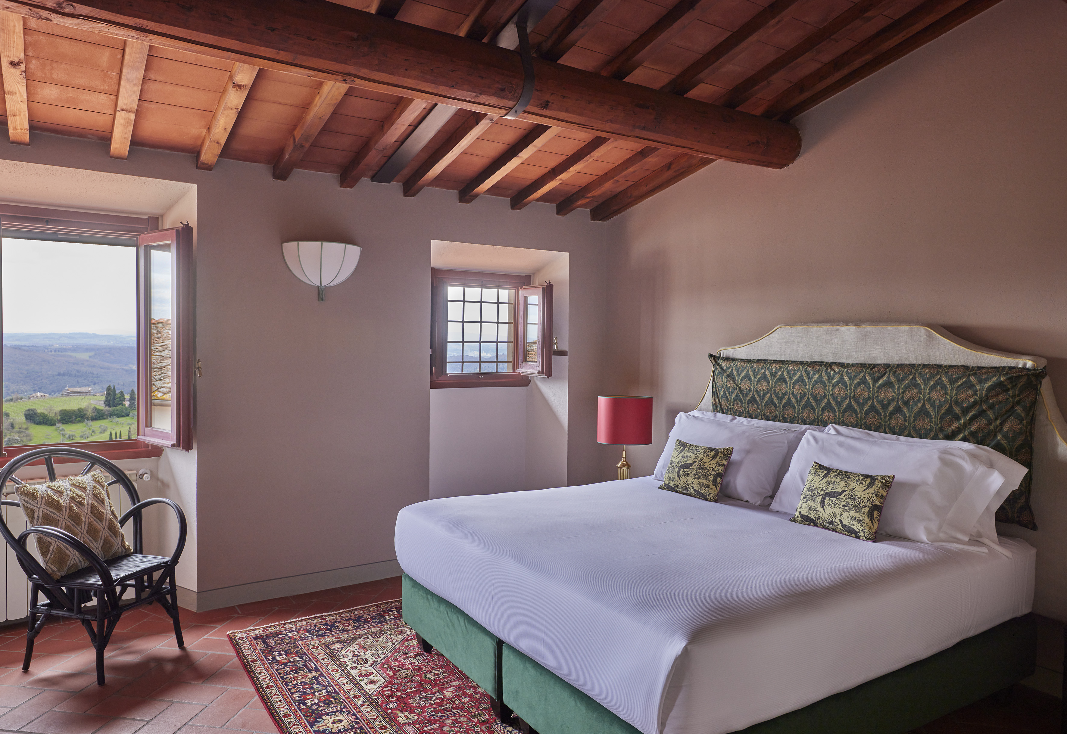 Rustic Tuscan bedroom with beamed ceiling, patterned rug, and scenic countryside views.