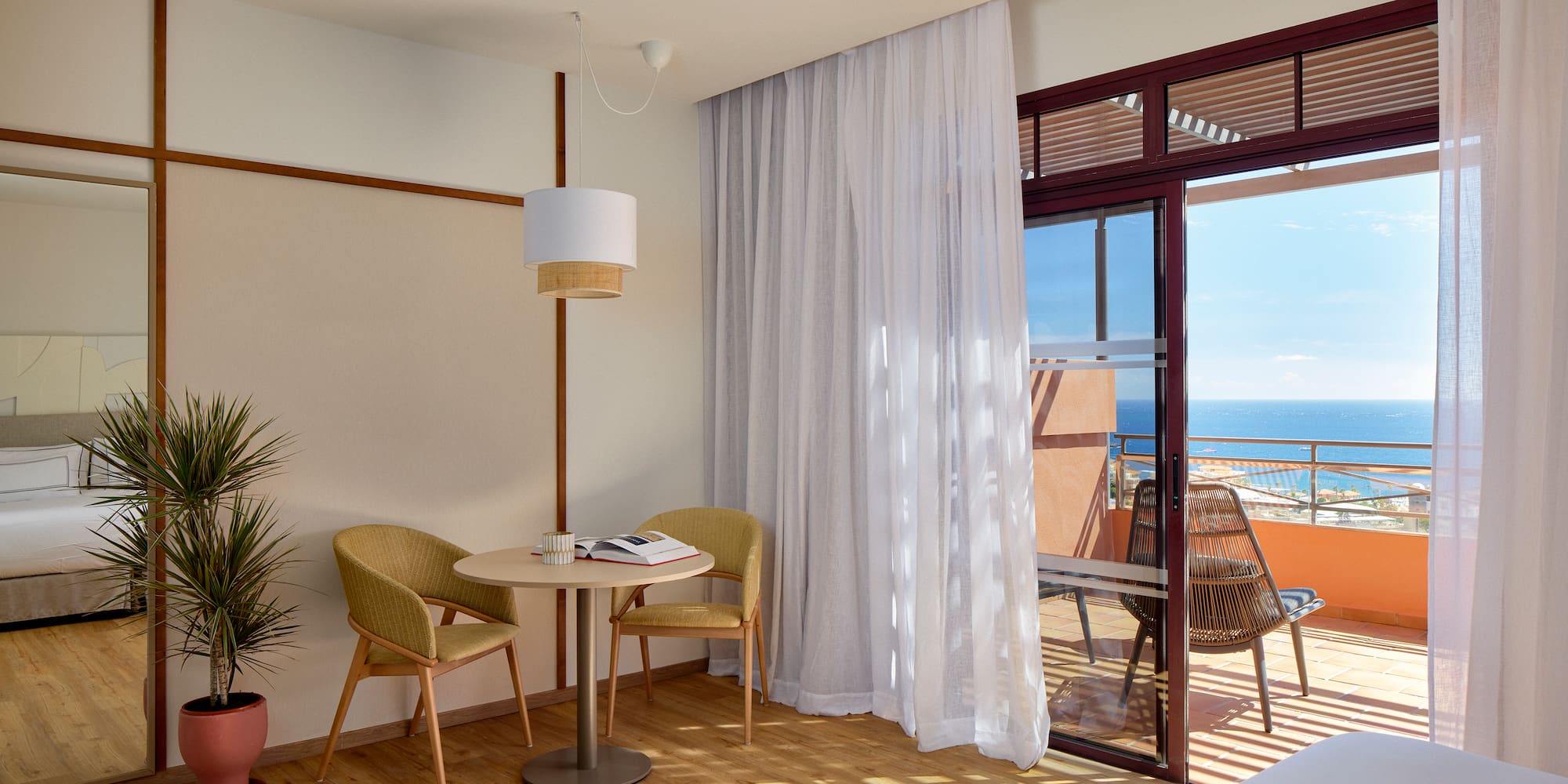 a room with a table and chairs and a balcony overlooking the ocean