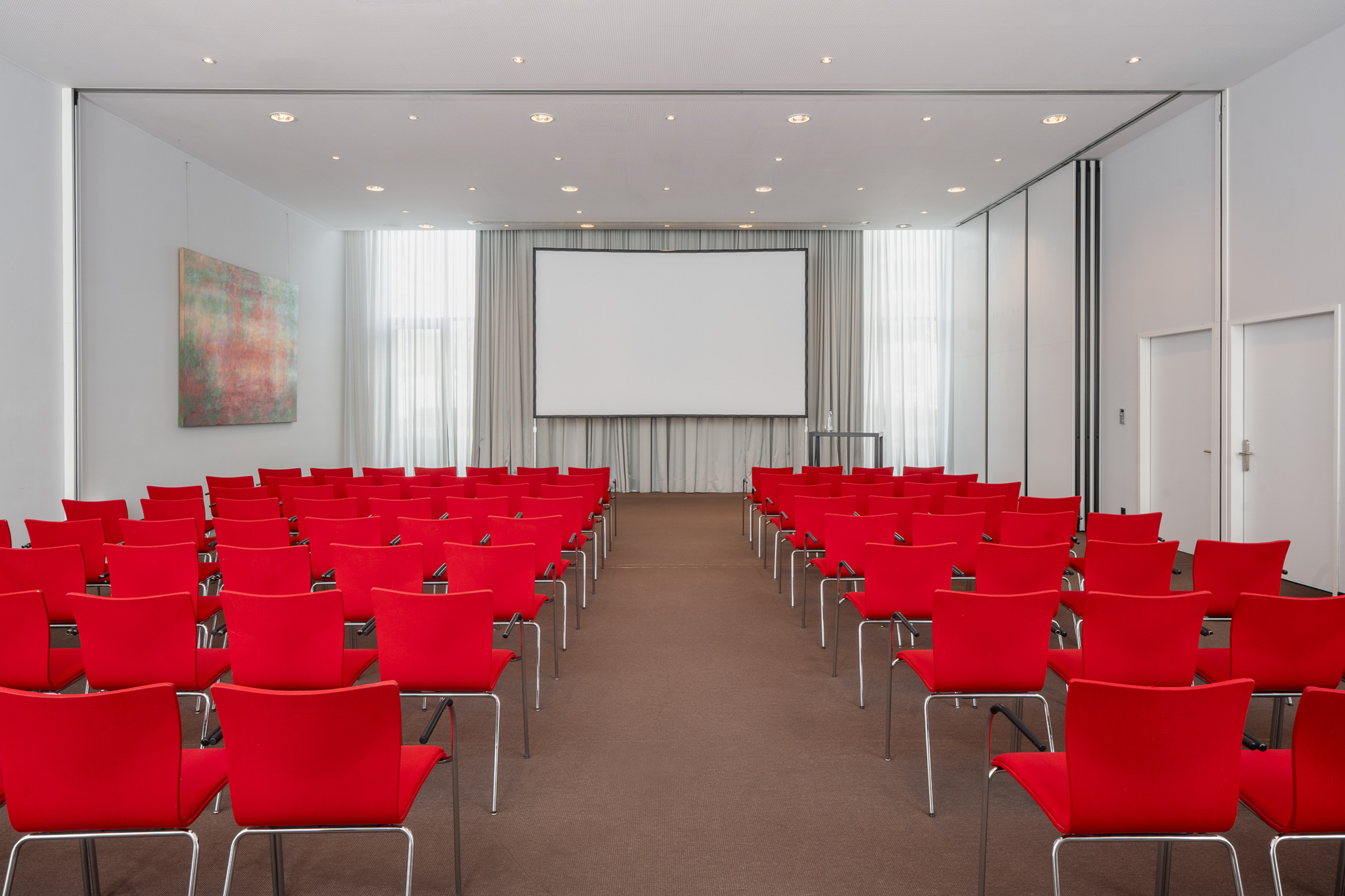 Modern conference room with rows of red chairs and a large projection screen.