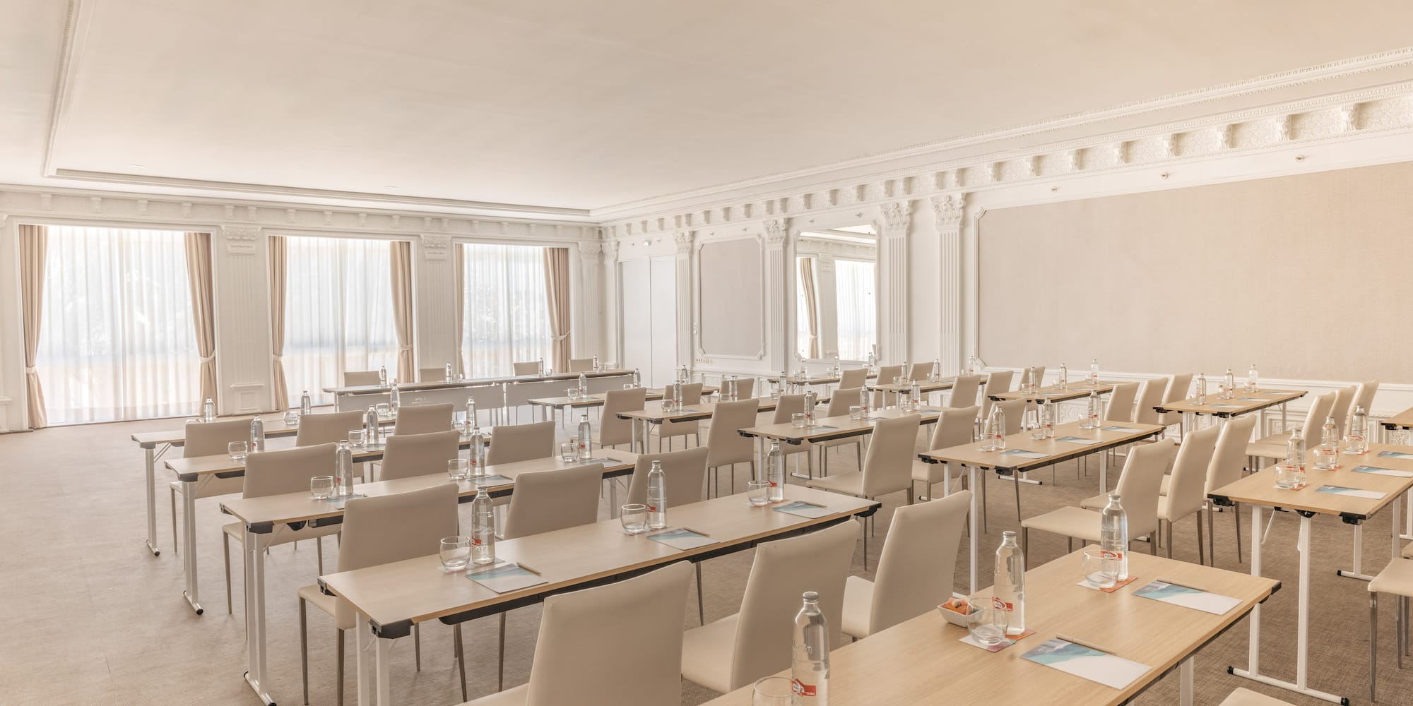Spacious, elegant conference room set up with tables, chairs, and water bottles.