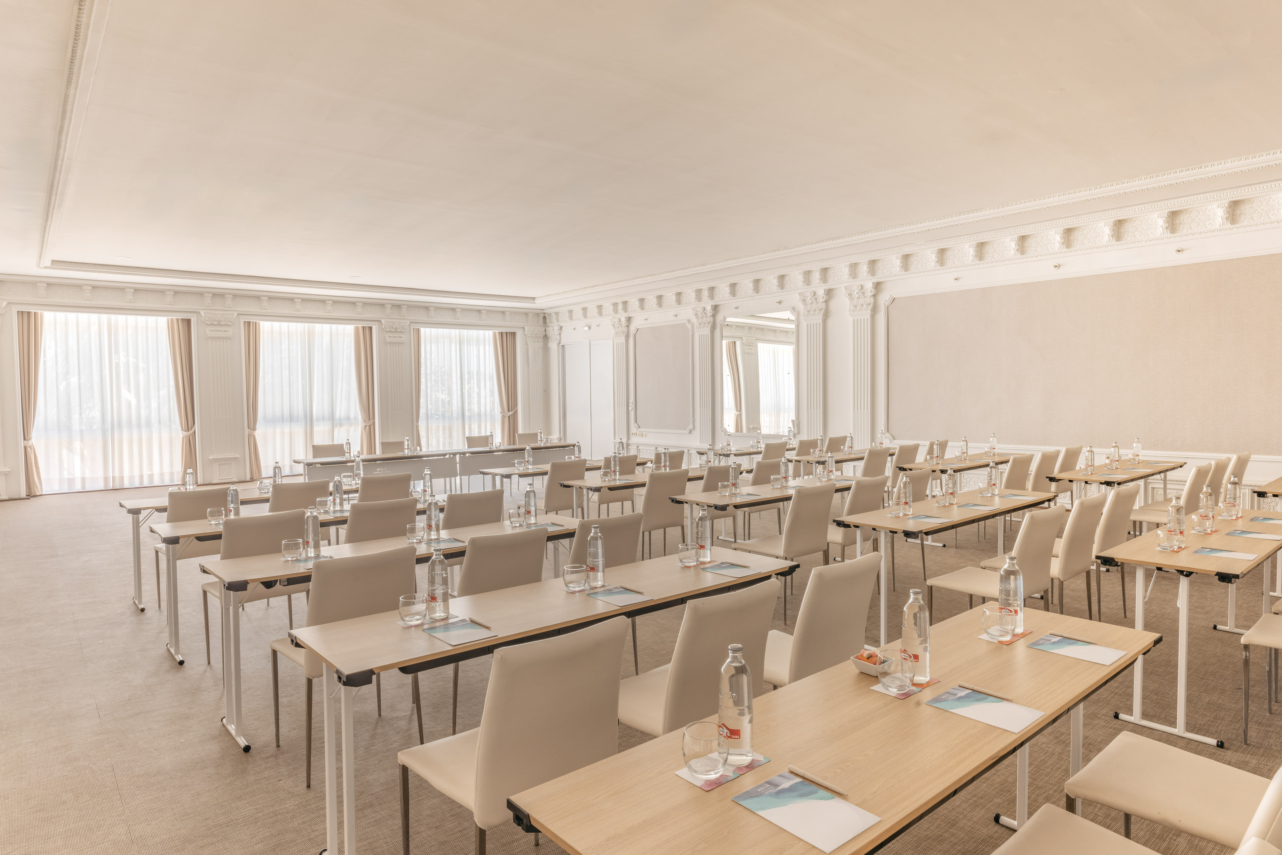 Spacious, elegant conference room set up with tables, chairs, and water bottles.
